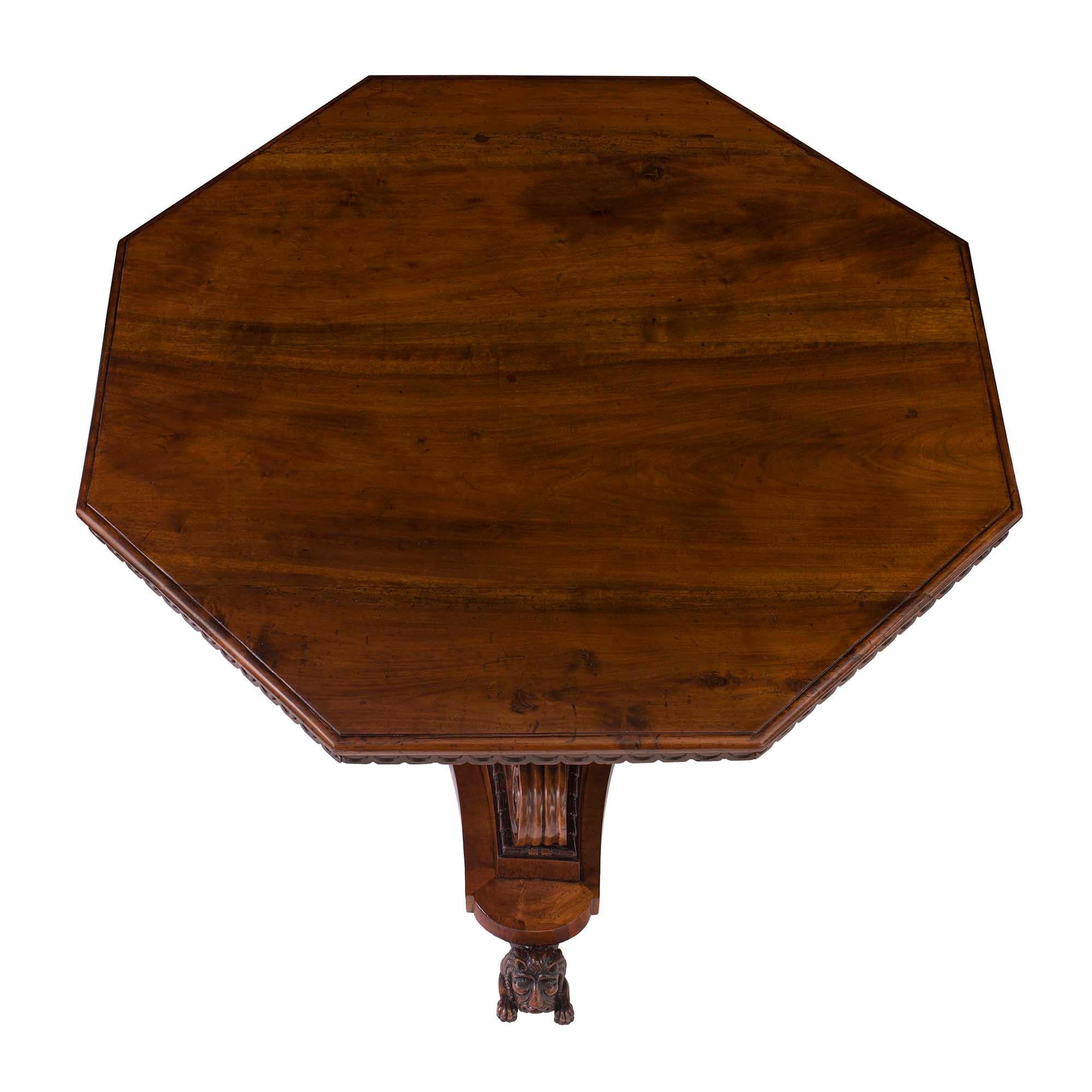 A monumental Italian 18th-century Tuscan octagonal walnut center table. The table is raised on three intricately carved lion-shaped feet below a fluted triangular base with concave sides. Above each of the three lions, a substantial scrolled carving