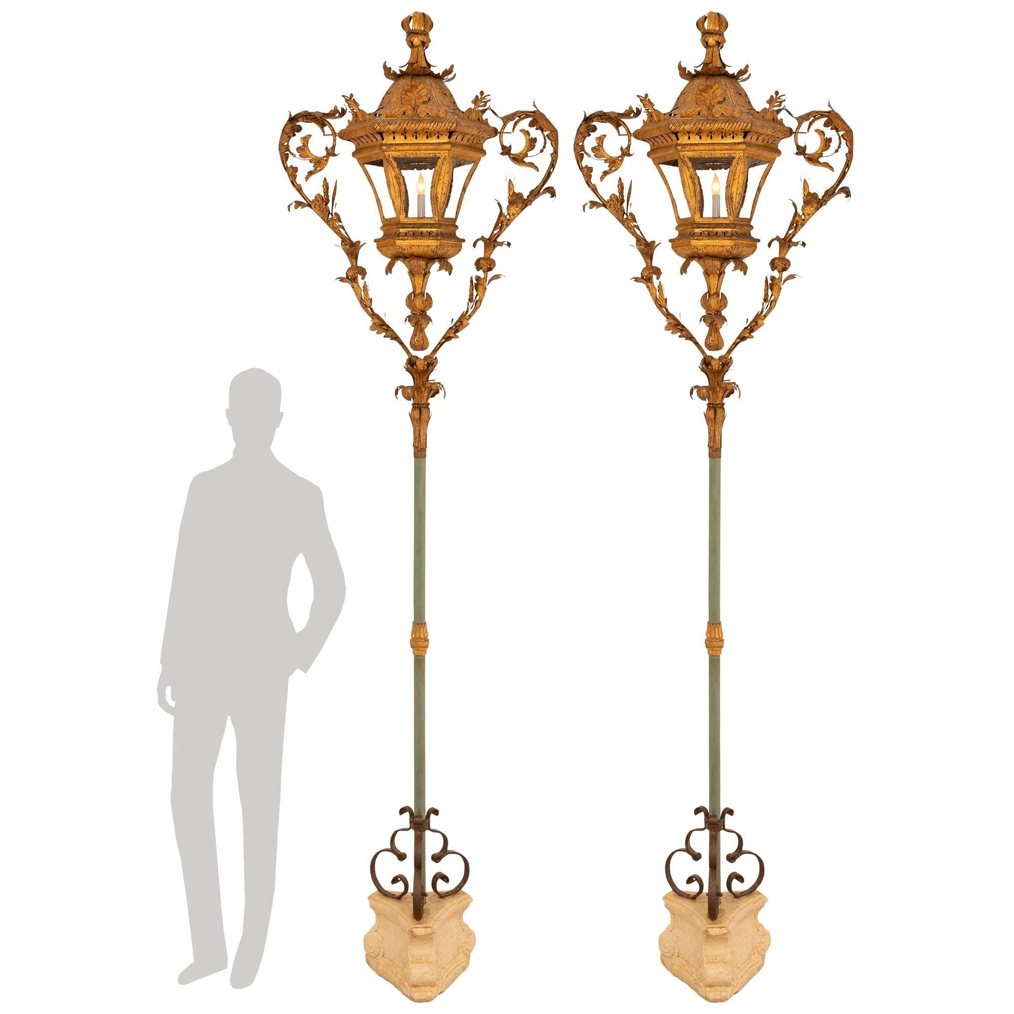 Un par extremadamente decorativo y único de faroles italianos del siglo XVIII de estilo veneciano, de metal dorado, madera patinada, hierro forjado, cristal y piedra. Cada farol de una luz, de elaborado diseño, se eleva sobre una base triangular de