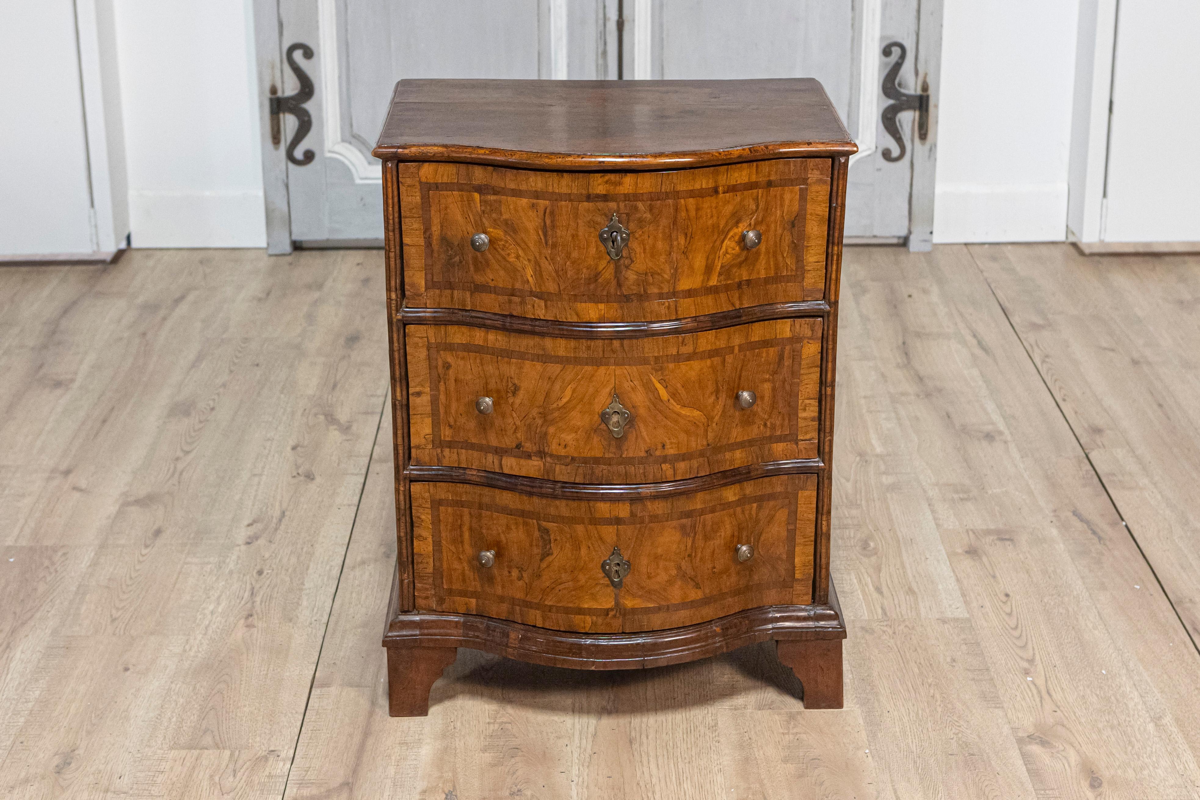 An Italian walnut and mahogany three-drawer chest from the 18th century with serpentine front, aged bronze hardware and bracket feet. Immerse yourself in the allure of the 18th century with this Italian walnut and mahogany three-drawer chest. The