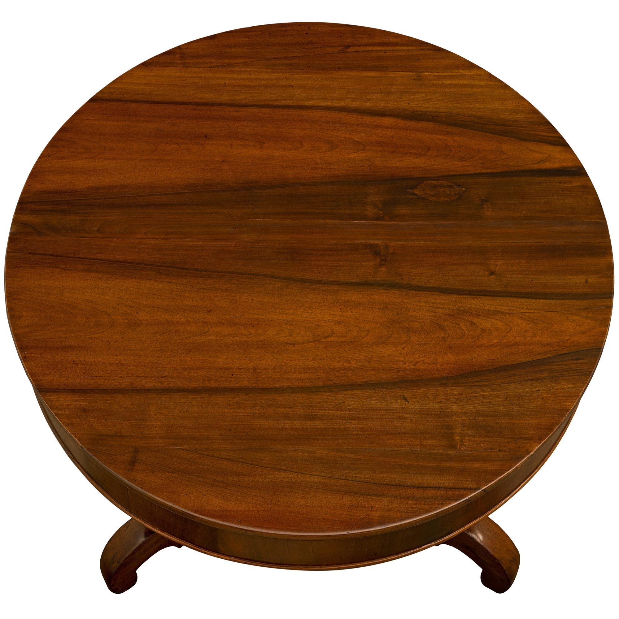 A handsome Italian 18th century walnut center table from Tuscany. The table is raised by three scrolled carved legs below a triangular central support with concave sides and richly carved recessed panels. The handsome top has a curricular apron and