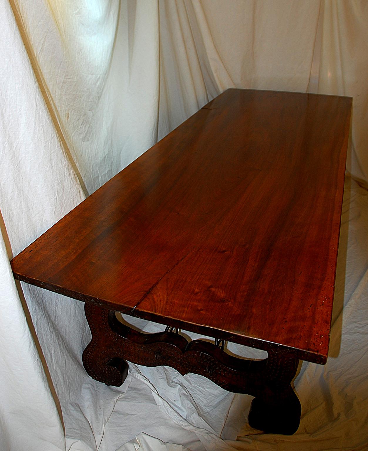 Italian 18th century solid walnut refectory table with chip carved pedestals and wrought iron twisted and curled stretchers. The stretchers start at the underside of the middle of the top and extend to the center of each pedestal. The block to which