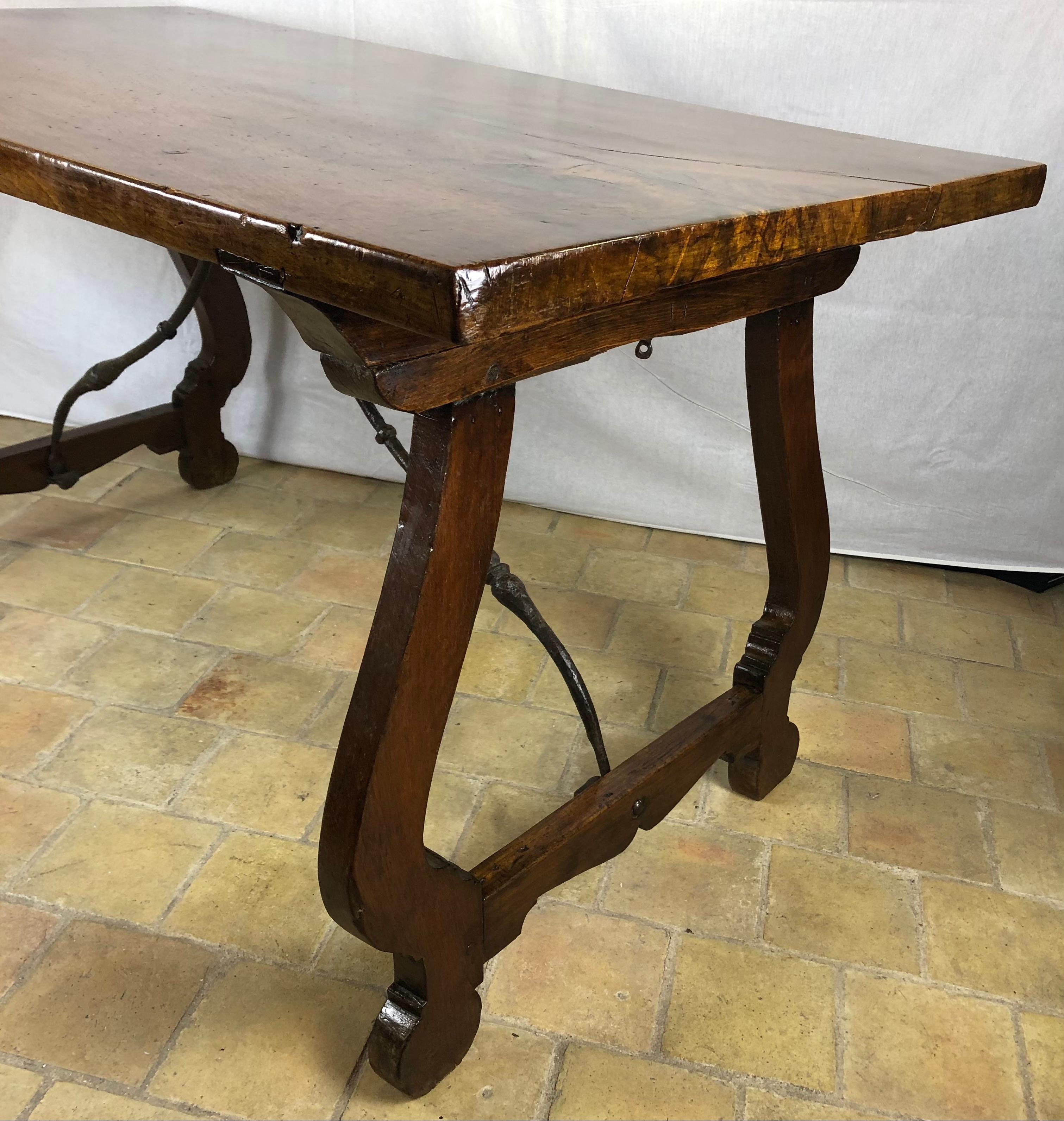A stunning Italian 18th century walnut trestle table. The table is raised by two sets of scrolled pierced supports connected by the original hand beaten wrought iron stretcher. Above is the elegant French polish walnut rectangular top constructed