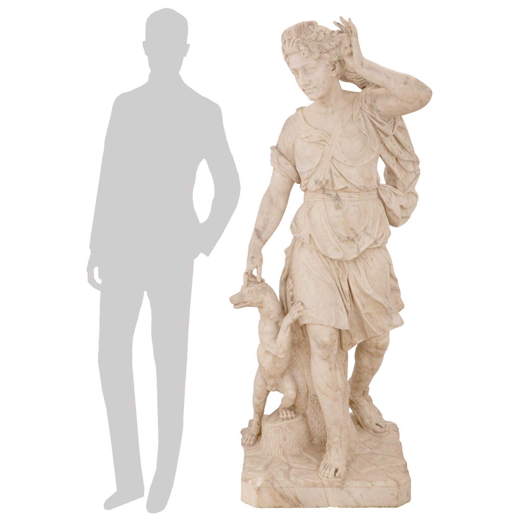 A stunning and extremely high quality Italian 18th century white Carrara marble statue of Diana and her dog. The statue is raised by an impressive thick square base with a wonderfully executed paved design and a finely detailed tree trunk at the