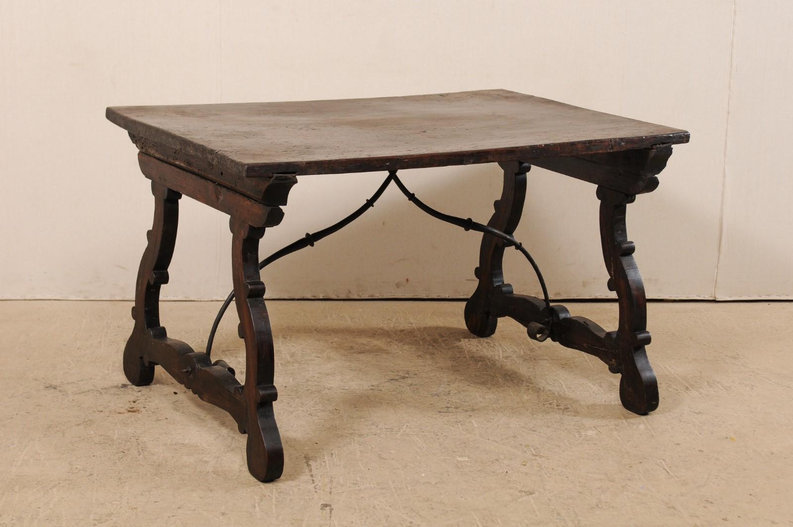 A late 18th century Italian trestle table with iron stretcher. This antique table from Italy features a rectangular-shaped top from a single piece of walnut wood, which is raised upon a pair of fluidly-carved trestle styled legs at either end. The