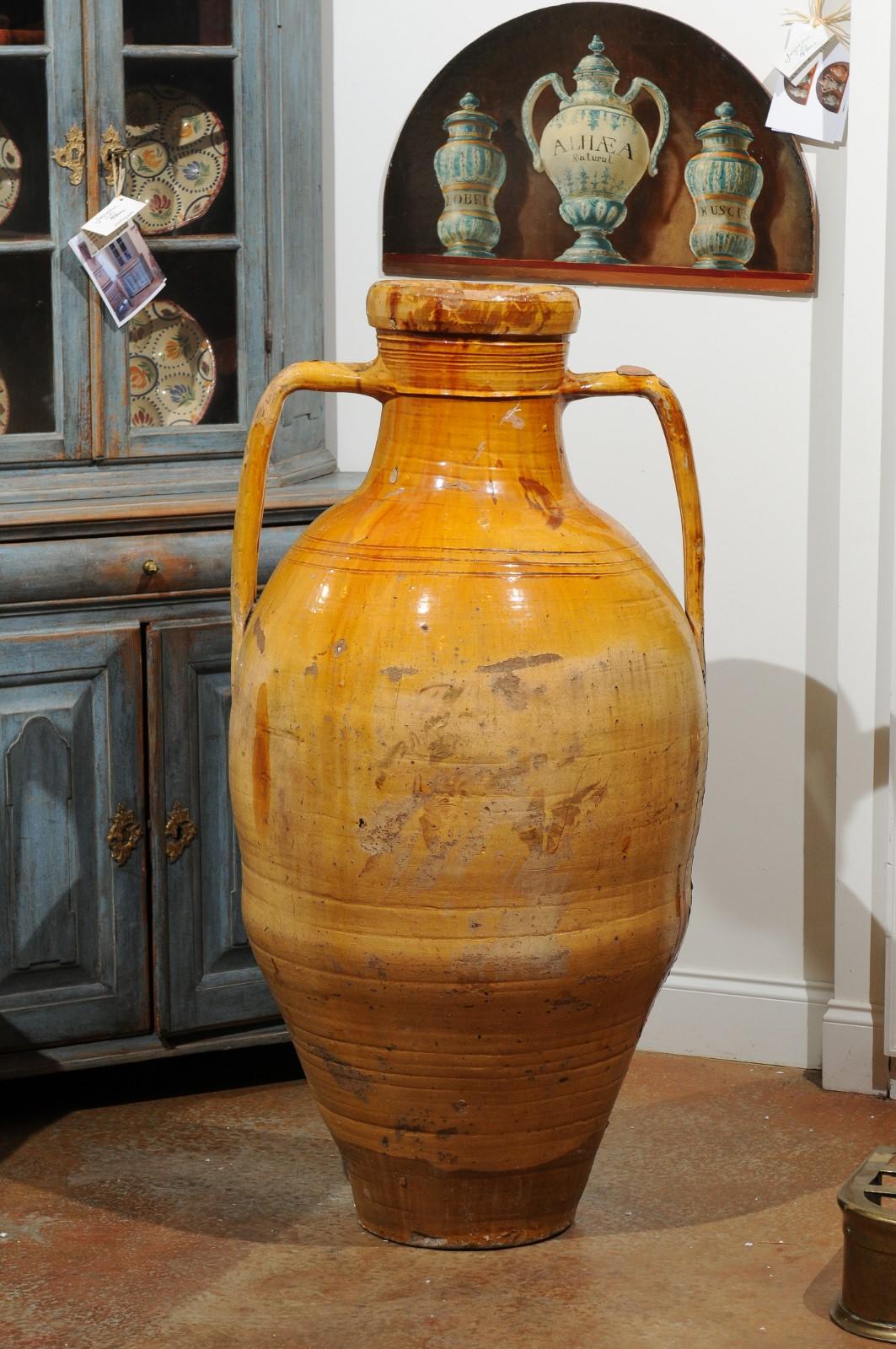 An Italian yellow glazed olive oil jar from the 18th century, with double handles and front spout. Created in Italy during the 18th century, this olive oil jar charms us with its yellow glaze accented with drips, and its tall silhouette flanked with