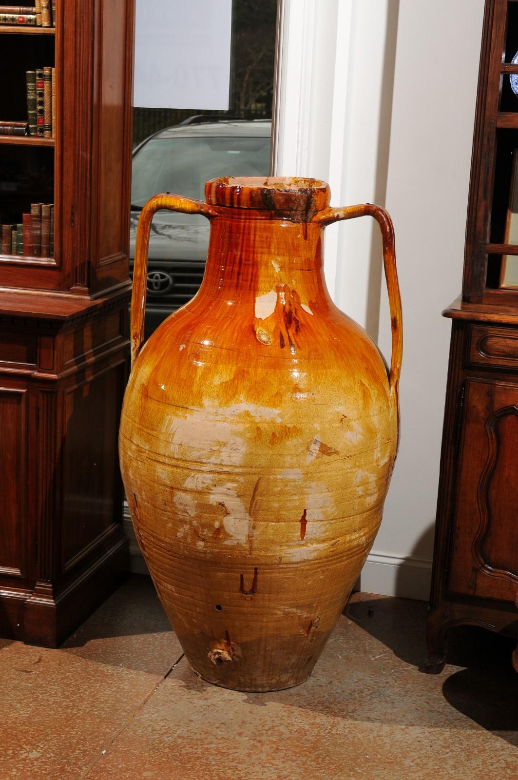 An Italian yellow glazed olive oil jar from the 18th century, with two handles and nicely distressed appearance. Handcrafted in Italy during the 18th century, this rustic olive oil jar is boasting a nicely weathered patina. The tall circular