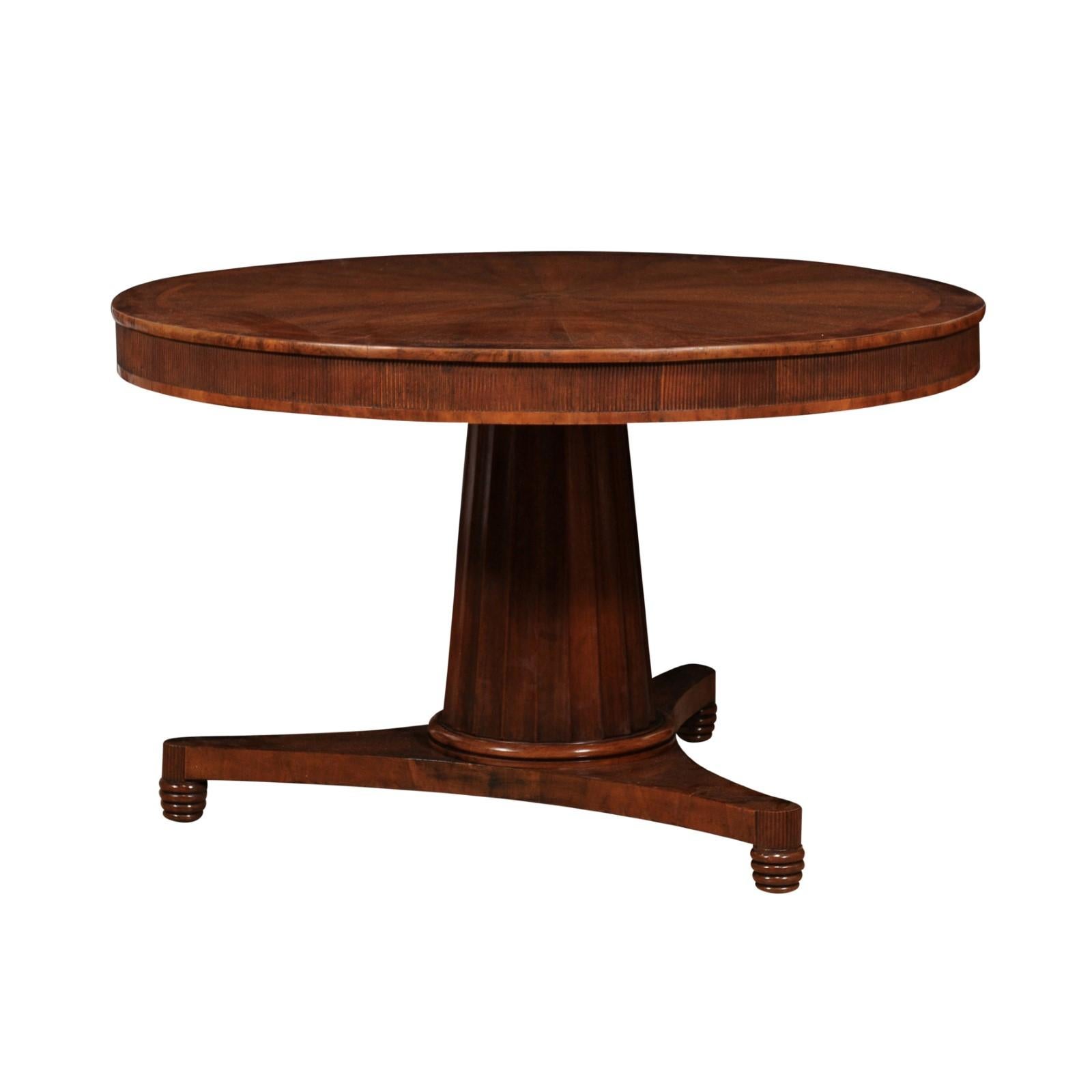An Italian Turn of the Century walnut pedestal center table from circa 1900, with radiating veneer on the circular top, carved reeded apron, two small drawers and tripod base. Elevate your living space with the distinctive character of this Italian