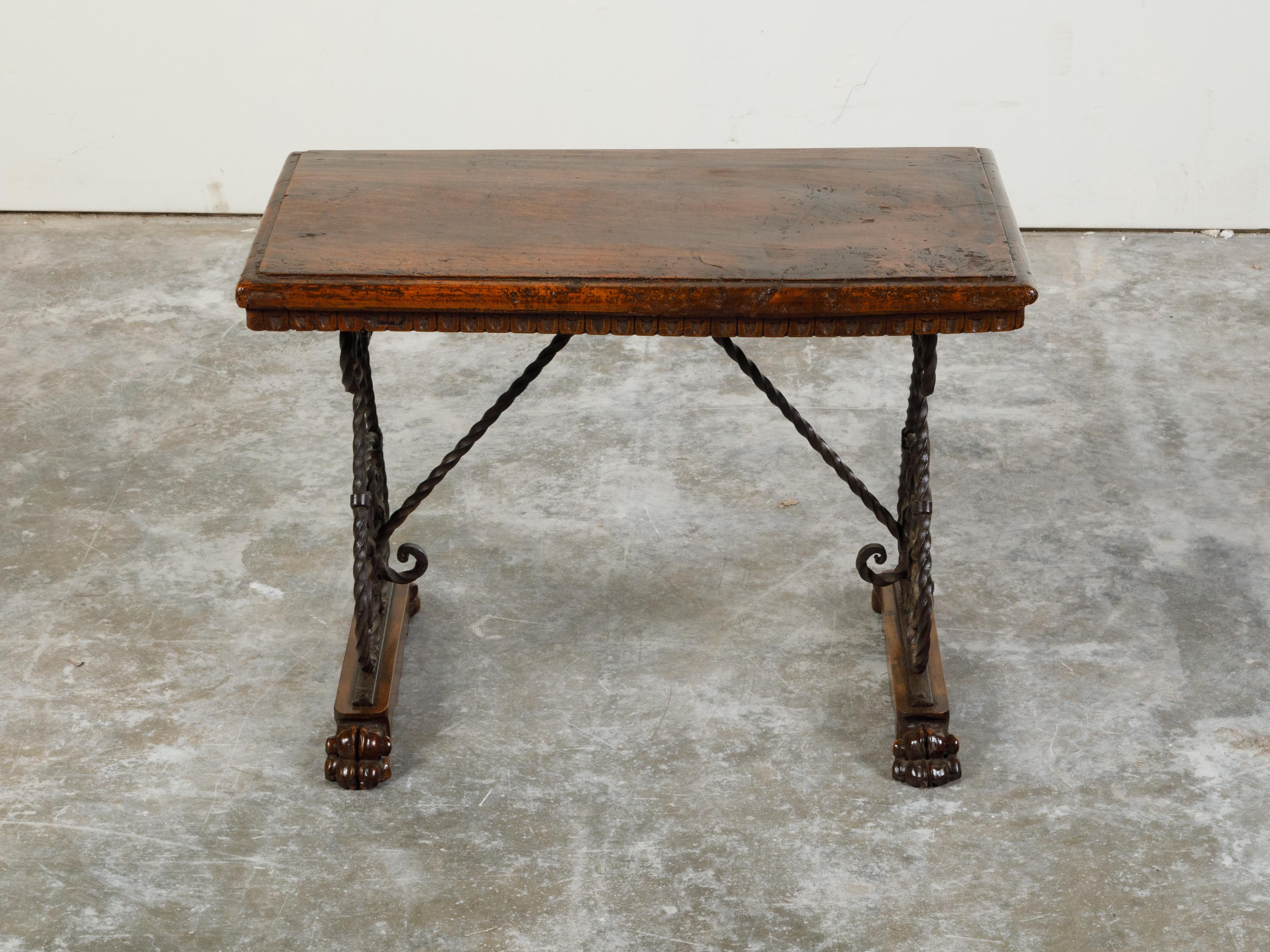 An Italian walnut and iron console table from the early 20th century, with scrolling base and fleur de lys motifs. Created in Italy during the early years of the 20th century, this console table features a rectangular wooden top with carved scoop