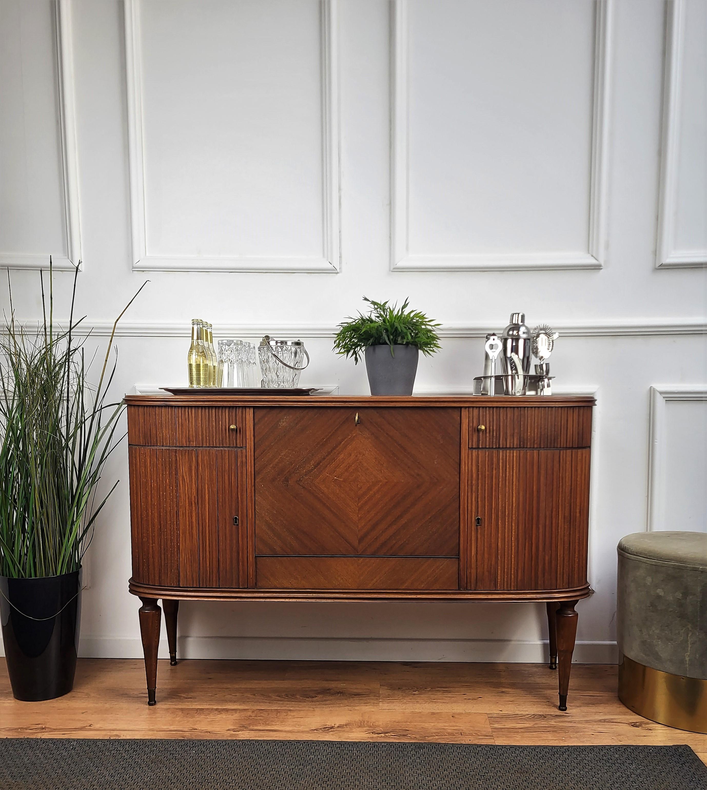 Very elegant Italian Art Deco Mid-Century Modern drinks dry bar cabinet with beautifully carved slatted walnut wood, two curved side doors and central drop-leaf door. When opened, on the bottom right, left and center bottles and accessories storage