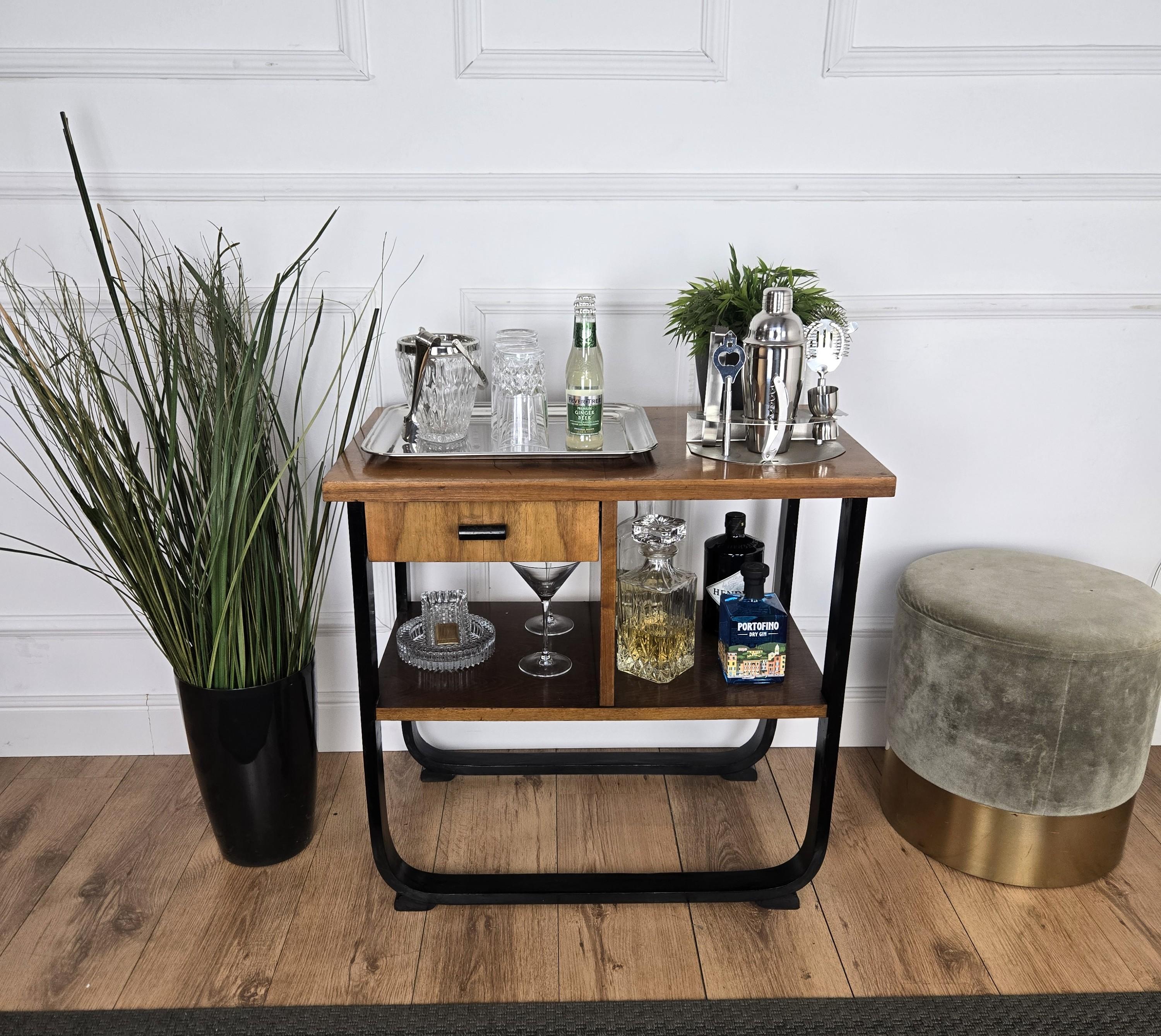 Very elegant Italian dry bar cabinet side table in typical Art Deco shape and materials with its beautiful wood, one drawer with typical deco' handle and the overall armonic curved main structure holding the shelves. The Art Deco style, that