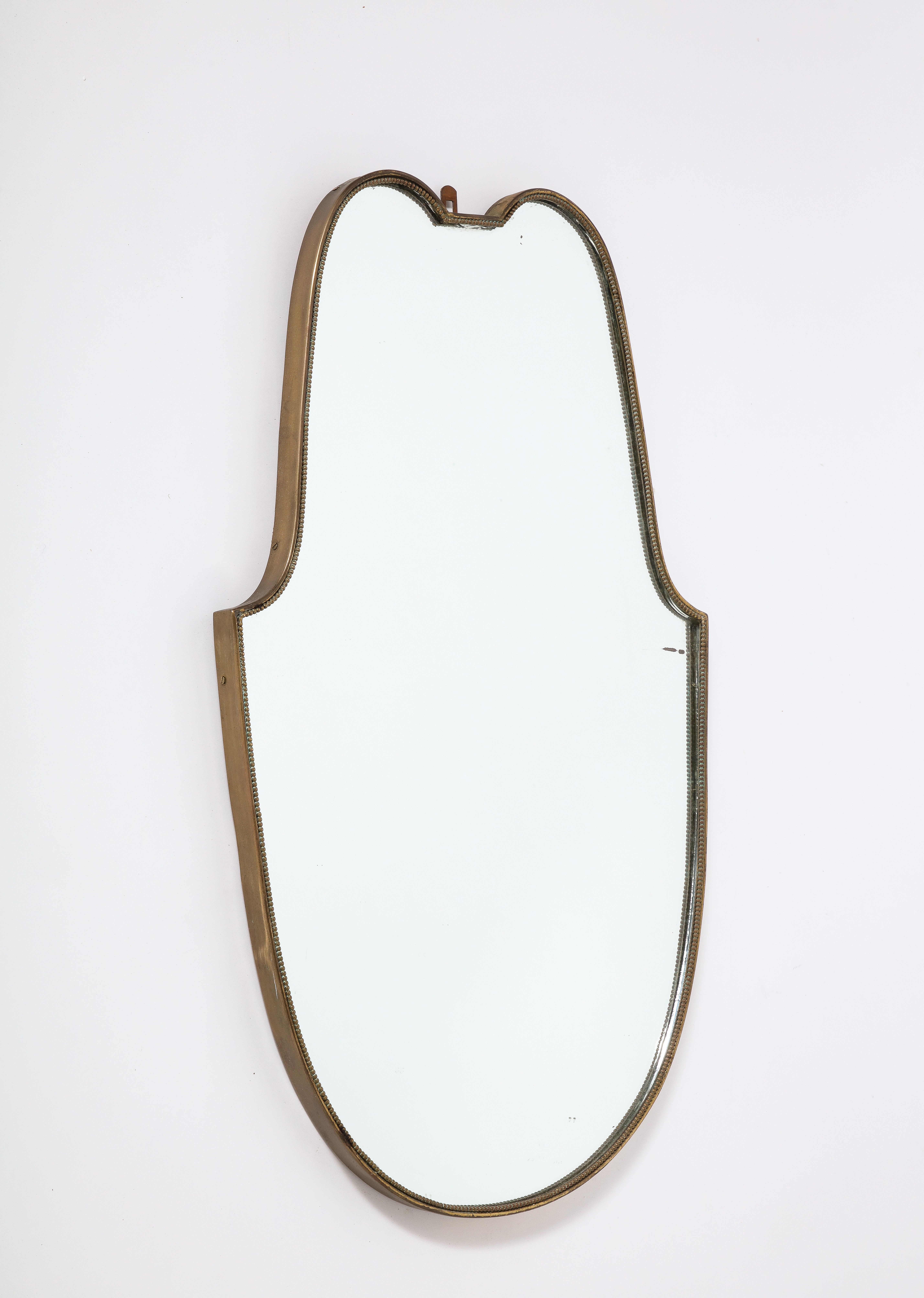 An Italian 1940's brass shield shaped mirror with beaded trim; the brass with a warm patina, mirror glass plate original. 
Italy, circa 1940 
Size: 30 1/2