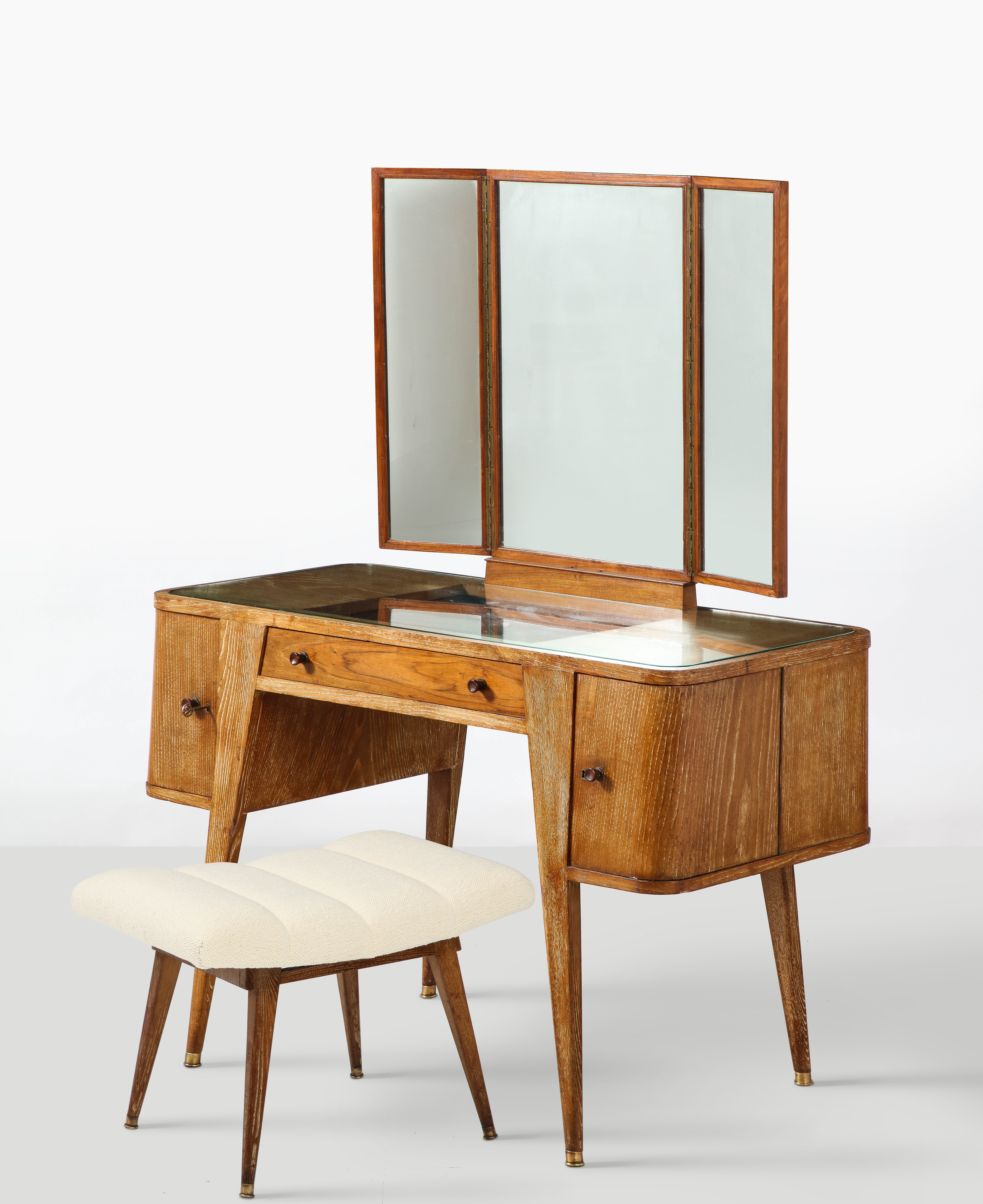 A rare and elegant Italian 1940's cerused oak vanity table and accompanying stool/bench. The vanity table has one drawer centered on the apron, with two curved corner doors on either end which open out, the right side door with two interior shelves