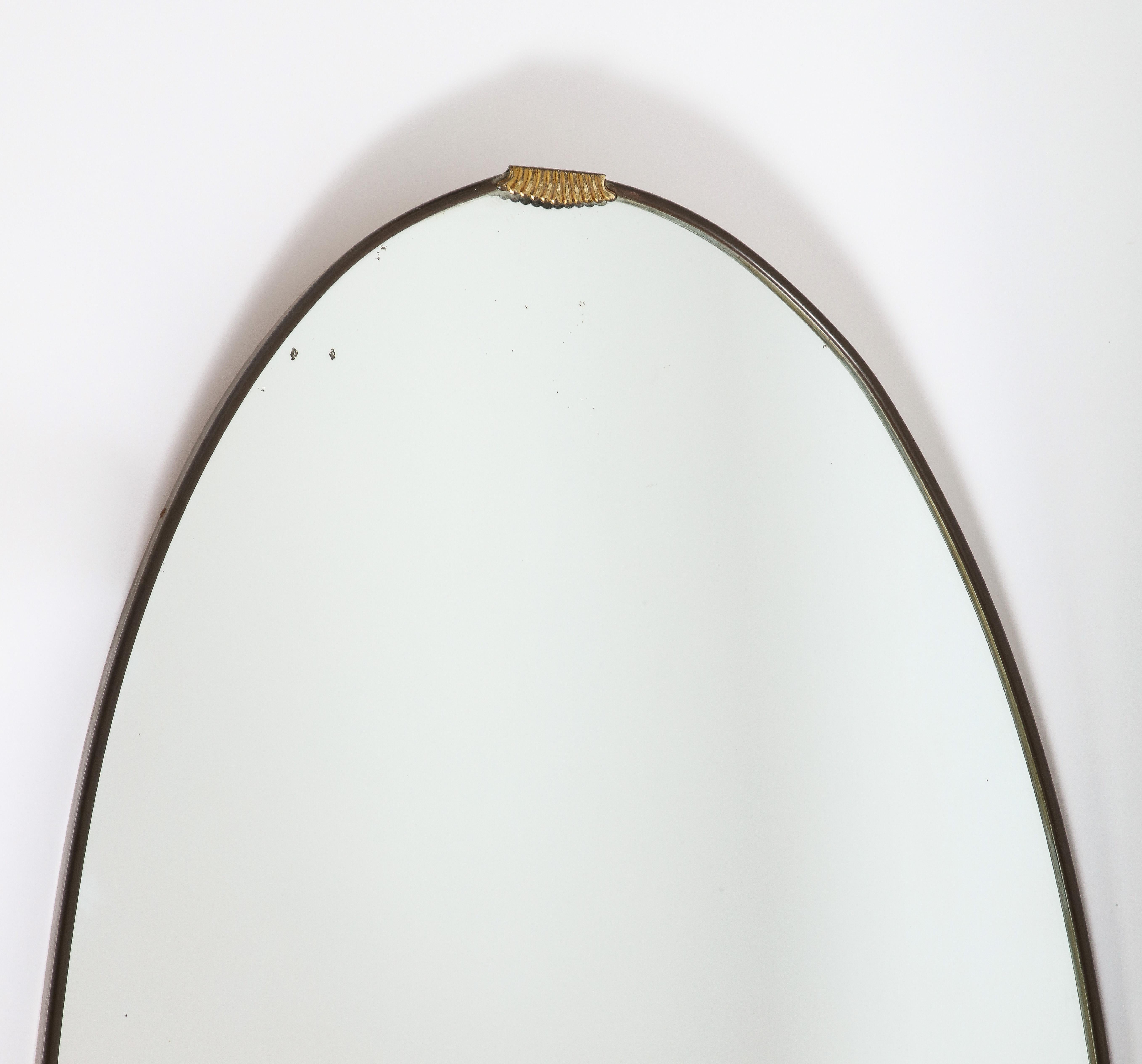 Miroir italien des années 1940, de grande taille, oblong ou ovale, en laiton, avec un magnifique décor de volutes en laiton sur la partie médiane de la partie supérieure.  Le laiton a sa patine d'origine et peut être nettoyé pour une finition plus