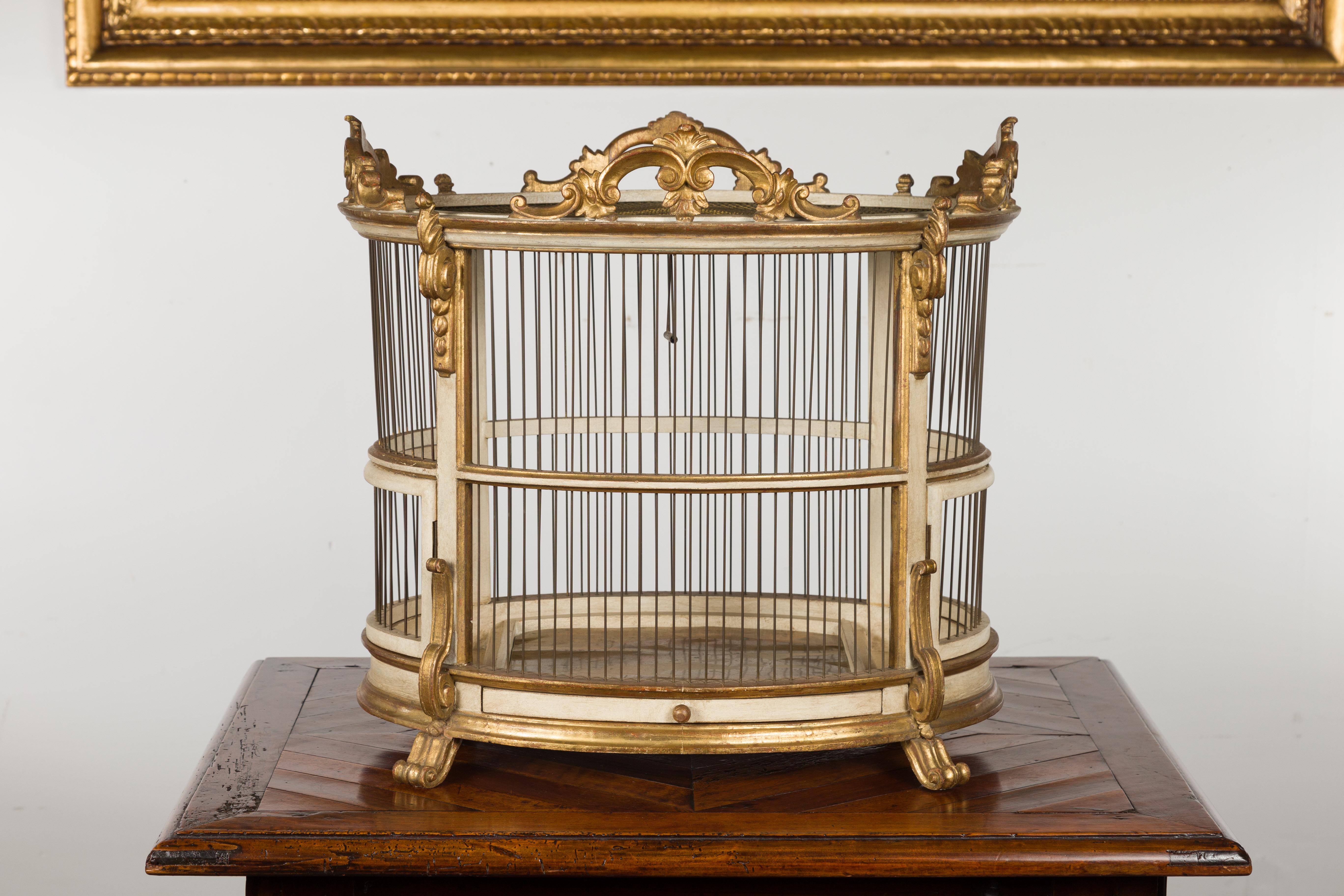 An Italian Rococo style birdcage from the mid-20th century, with gilt and painted accents. Created in Italy during the second quarter of the 20th century, this elegant oval birdcage charms us with its painted and gilt finish, perfectly complimenting