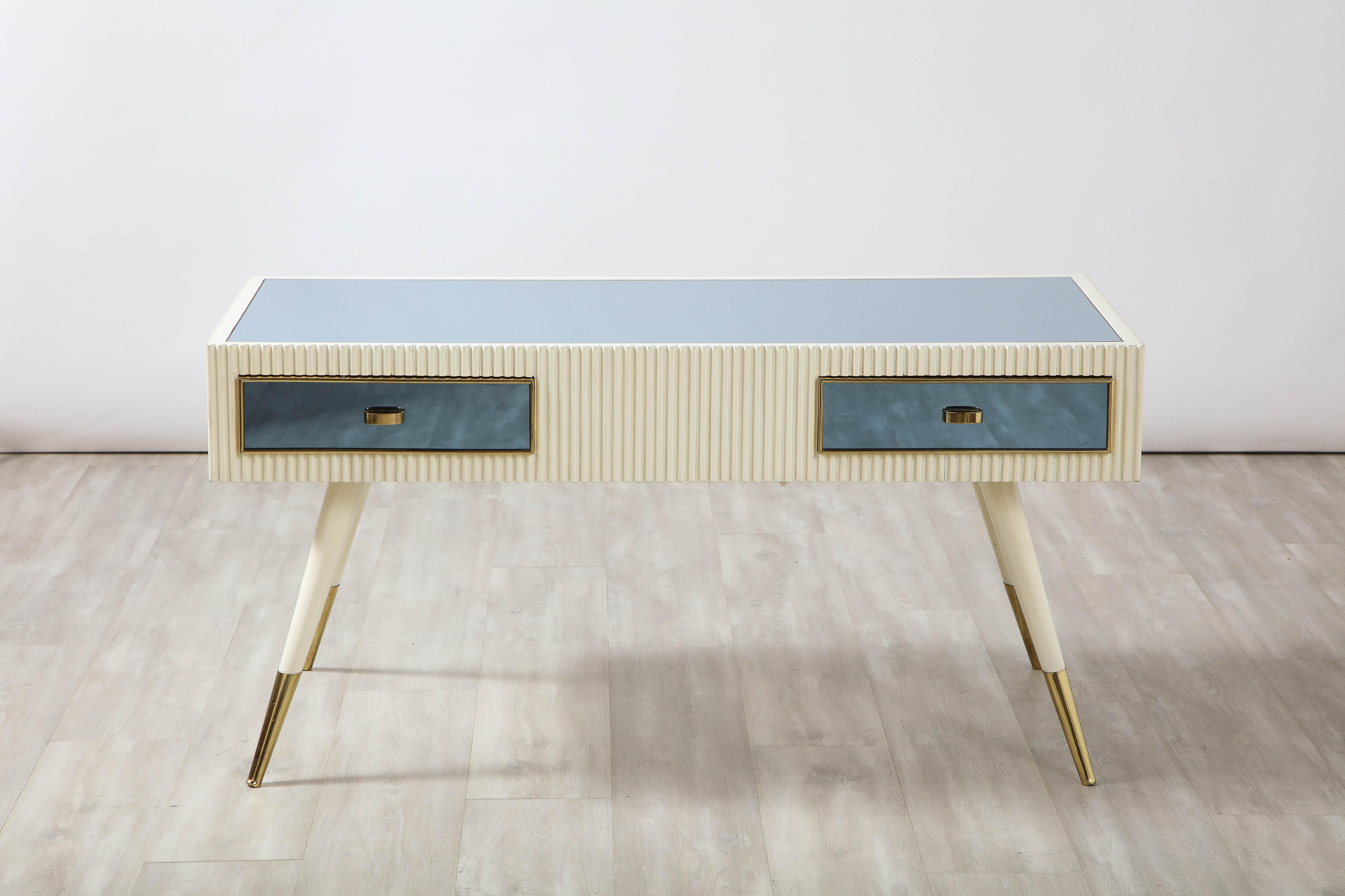 A highly unique Italian stylized coffee table, the surface with spectacular blue glass, the rectangular frieze with two drawers, also in blue glass with horizontal brass pulls and brass outline, the whole in creamy white hand-carved fluted design