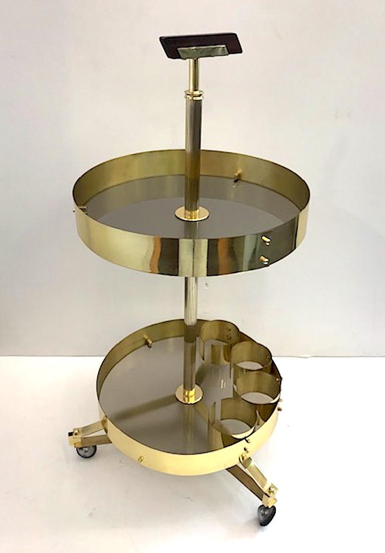 Chariot de bar rond en laiton et satiné des années 1950. Chaque étagère est constituée d'une plaque de verre fumée pâle satinée et est fixée au chariot en laiton. Poignée supérieure en bois. Base tripode avec roulettes supérieures chromées et roues