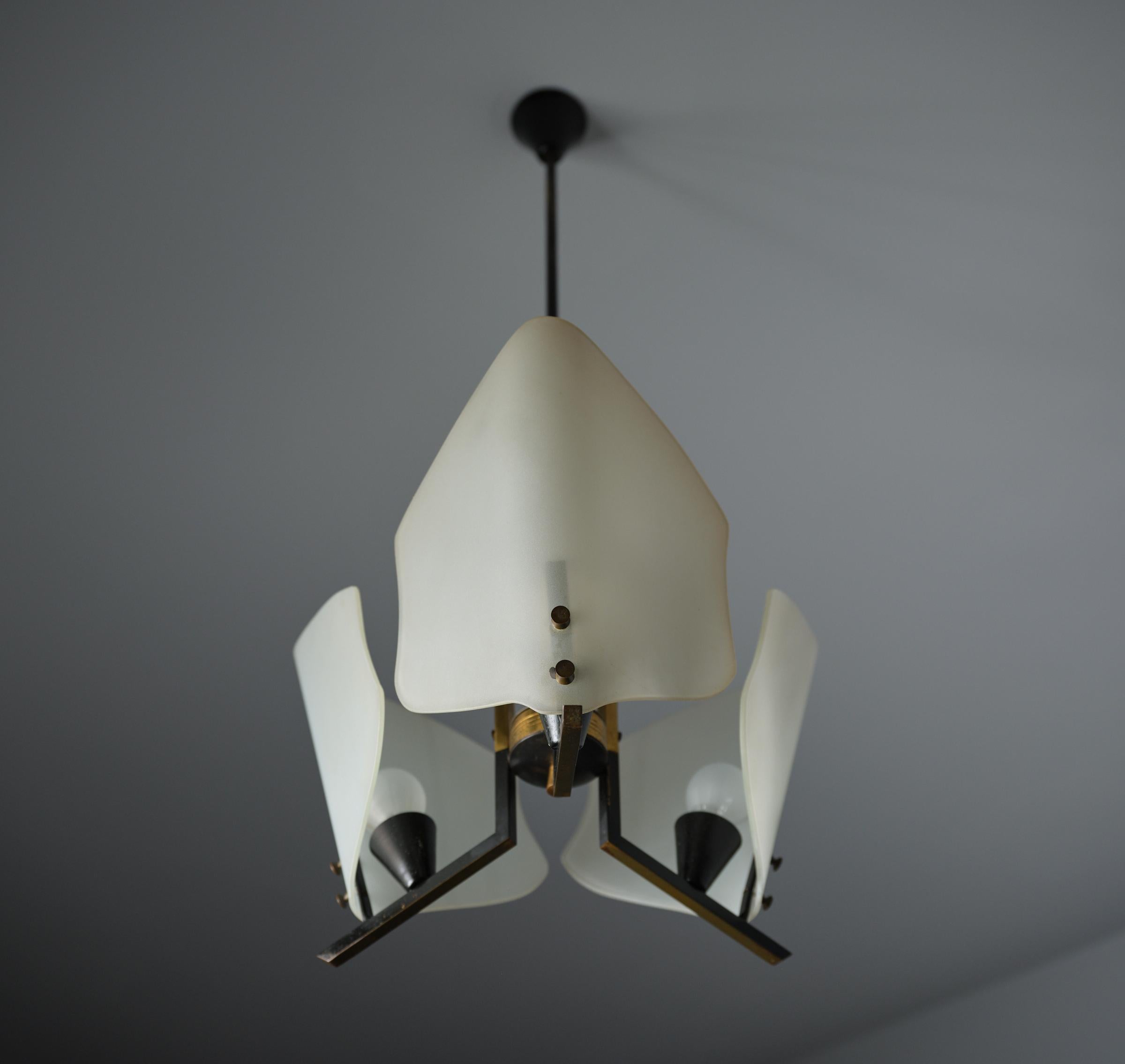 This chandelier embodies the elegance and refined Italian design of the 1950s. Featuring three points of light, each adorned with opal glass shades, it offers soft and inviting illumination. The structure, almost entirely crafted from brass,