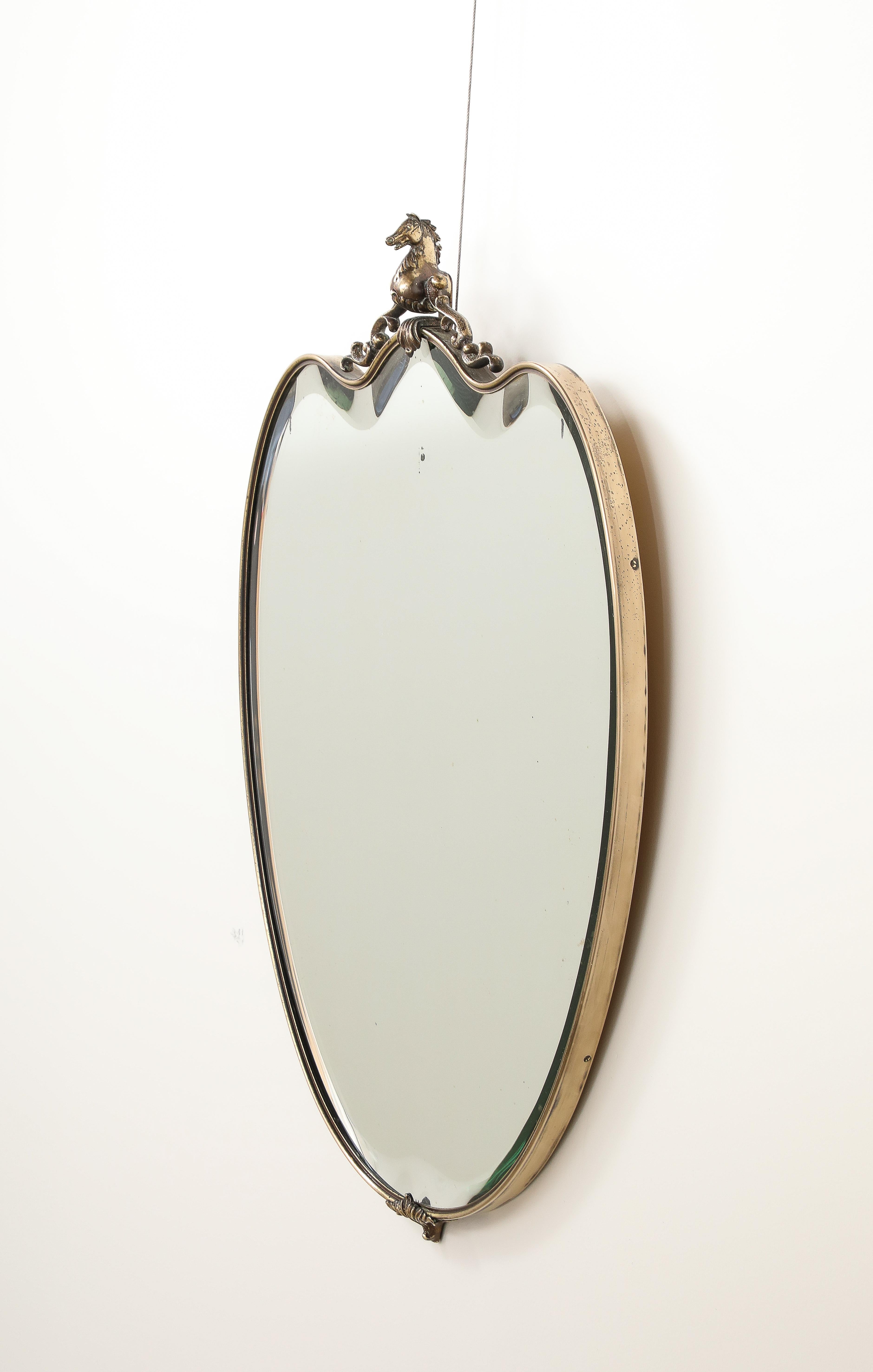 A highly unique Italian 1950's brass shield shaped wall mirror with a brass carved sculpture of a horse surmounted in the center.  With a thick beveled mirror plate and wonderful brass patina.  
Italy, circa 1950 
Size: 30