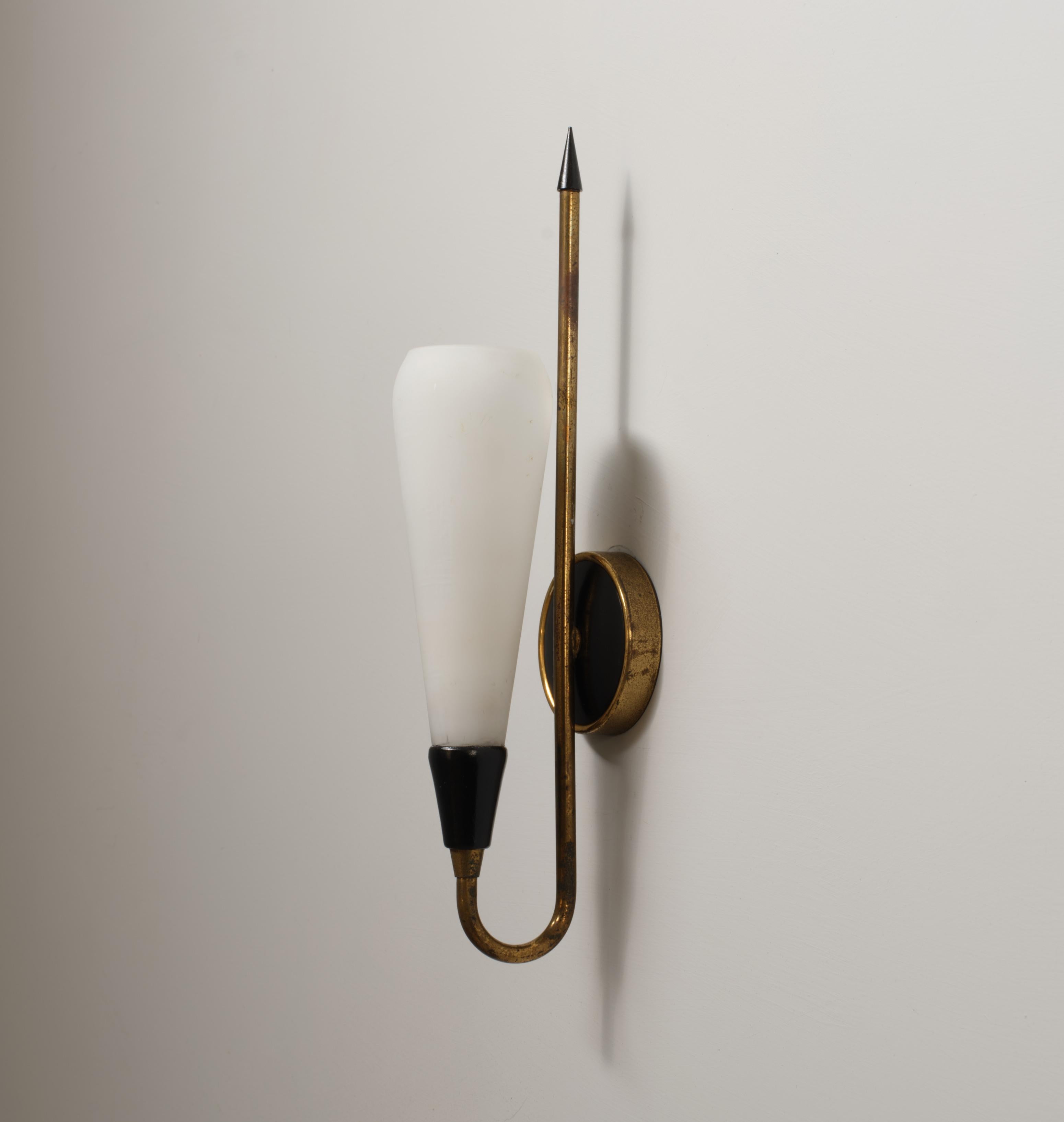 Wall-mounted sconce produced in Italy in the 1950s. The structure features a brass backplate, a curved brass arm with vertical extension terminating in a black metal finial, and a conical white opaline glass shade mounted in a black lacquered socket