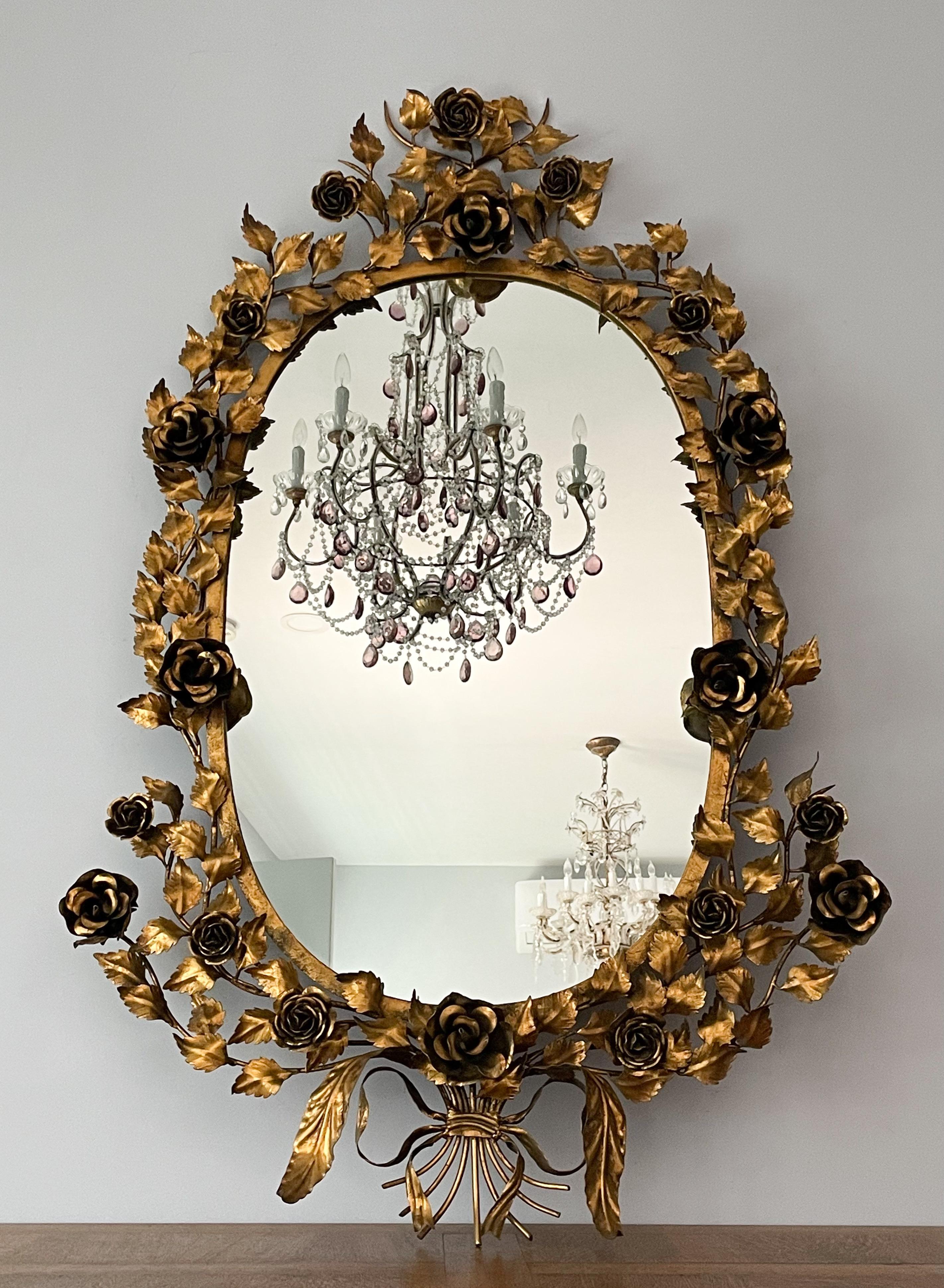 Fabulous, Italian 1950s gilt-tole painted iron mirror in the Hollywood Regency style. 

This impressive mirror consists of a detailed iron frame forged in the form of roses, foliage, a bow at center bottom and a glass mirror insert. 

Very chic