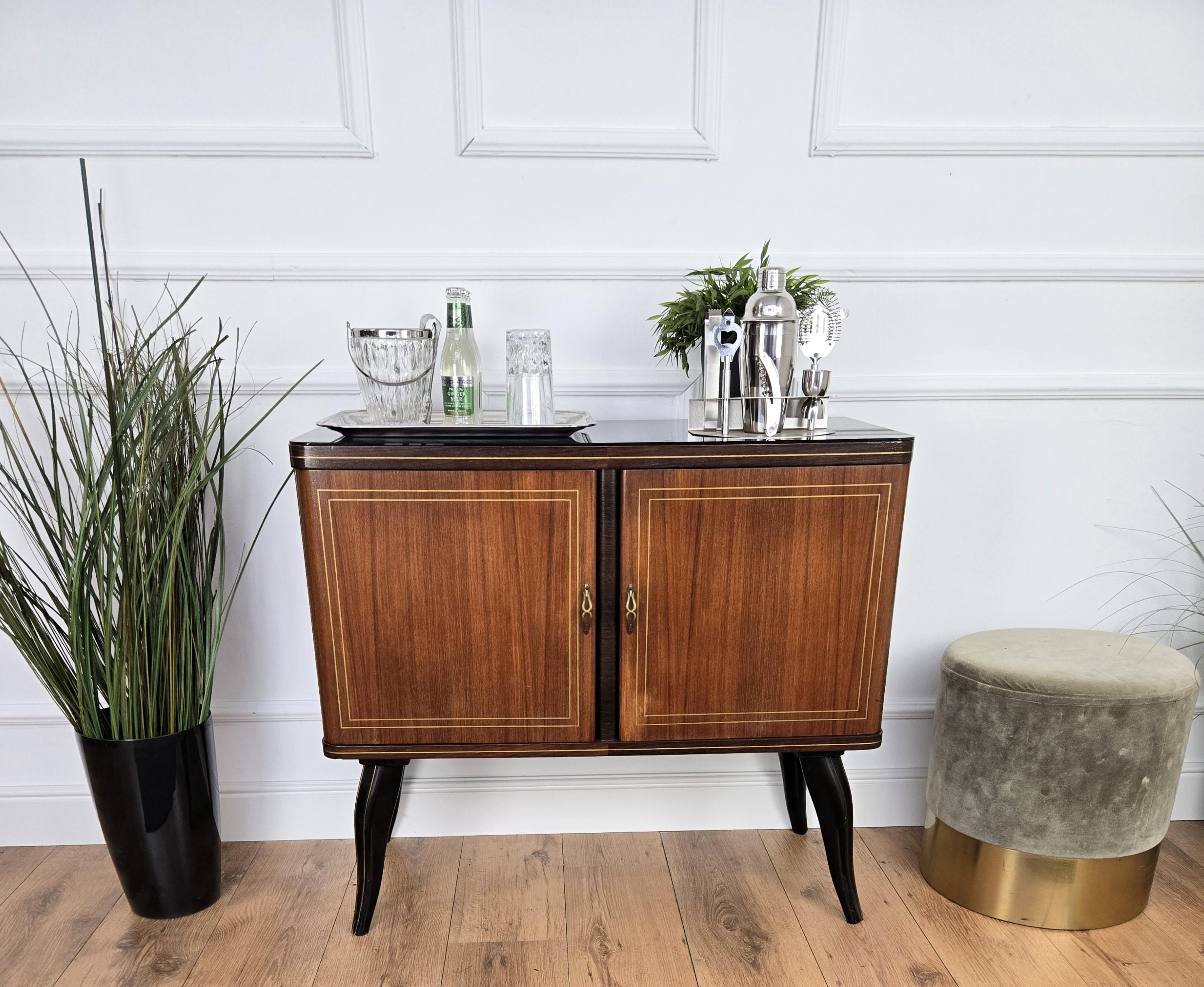 Very elegant Italian Mid-Century Modern drinks dry bar cabinet with beautiful wood, black glass top, two doors and great brass linear decors and handles. When opened, on the right side an amazing interior part in mirrors mosaic and glass shelf ideal