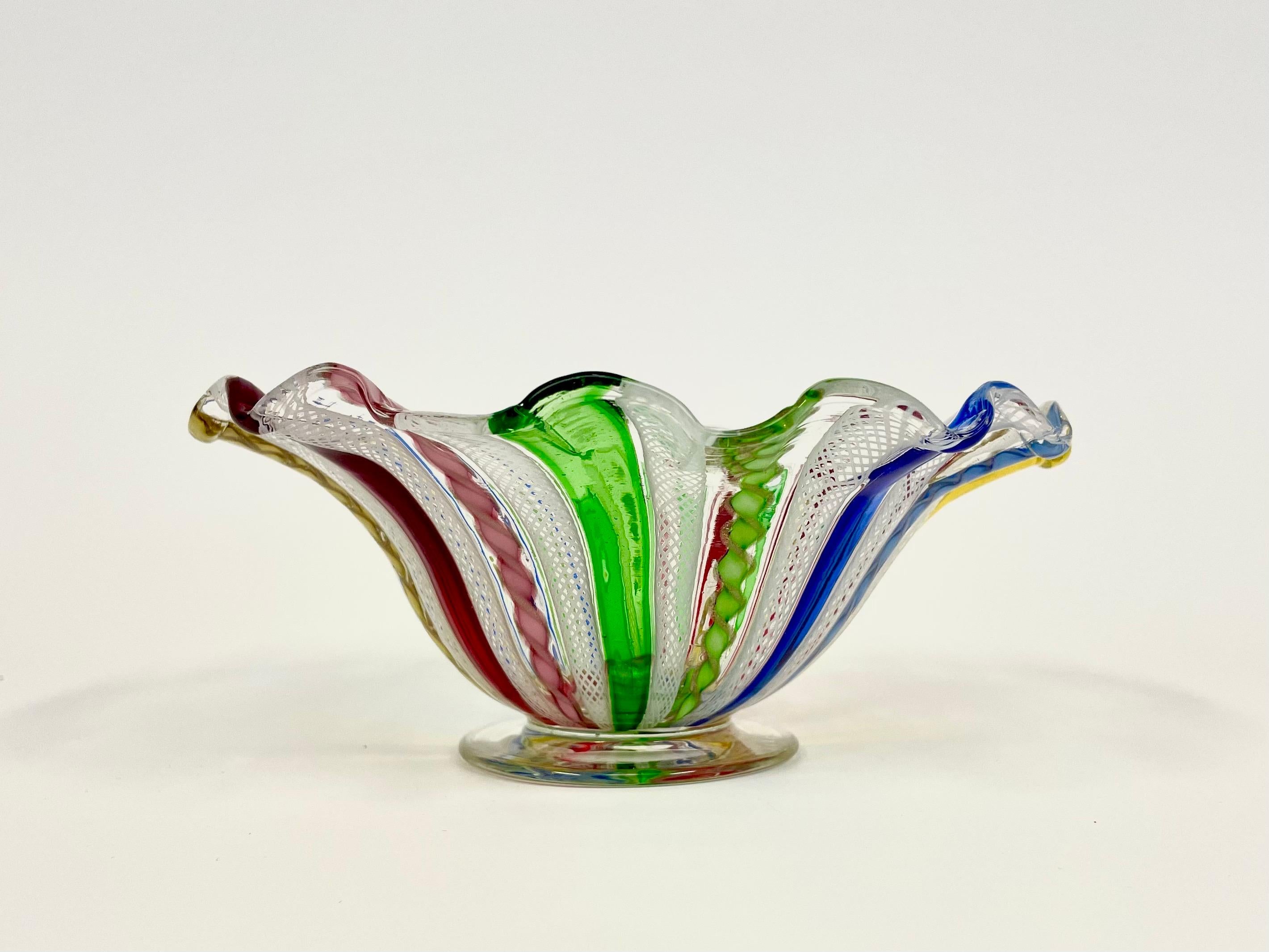 This is the Italian rainbow colored Venetian footed bowl in glass from Salviati, Murano. 
It comes decorated in colored translucent ribbons in blue, green, red and yellow on white foundation. 
Every other colored ribbon are twisted and sprinkled