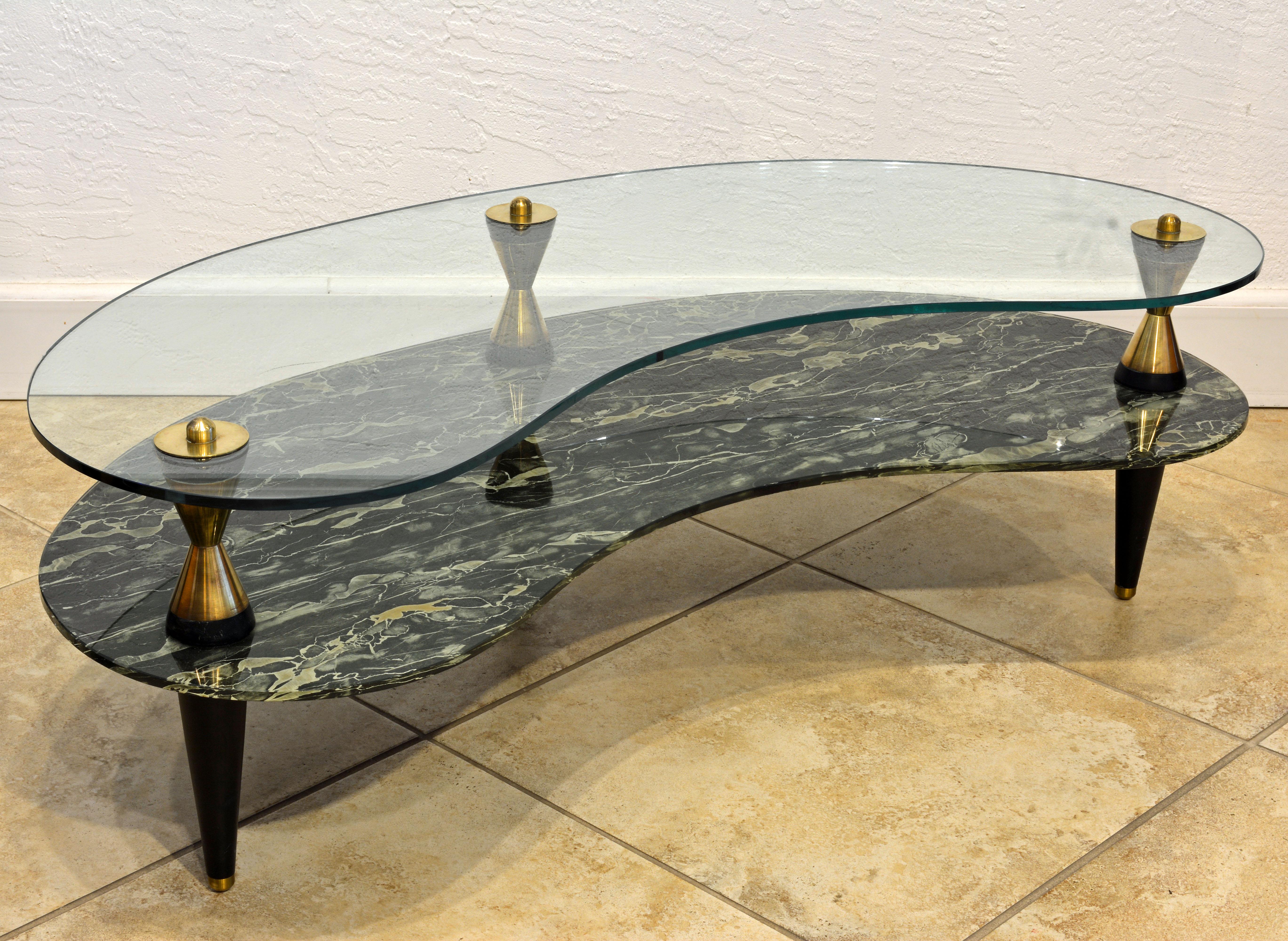 This typical midcentury sofa table features two kidney shape tiers, the top tier of clear tempered glass and the lower tier of tempered 'verre Églomisé' meaning painted on the back side. The legs are made with ebonized wood and solid brass cones and