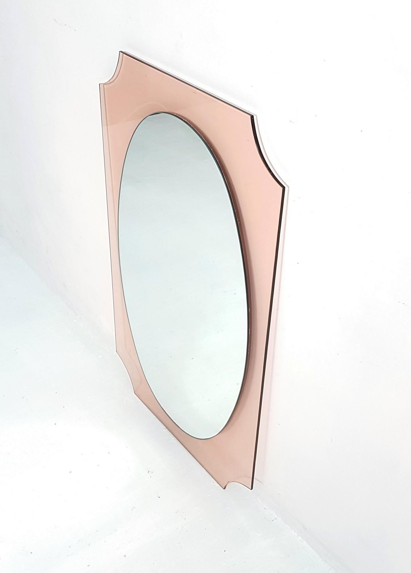 Italian wall mirror with an oval shape sitting on top of a backing of a square Smokey amber/pink colored Lucite with rounded corners.