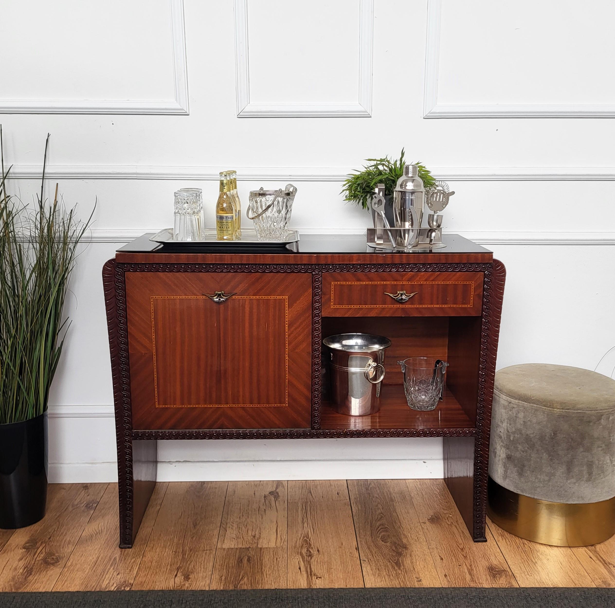 Très élégant meuble de bar à boissons sec Art Deco italien du milieu du siècle, avec un beau placage de bois décoré de noyer, un plateau en verre noir, reposant sur des pieds en forme de cascade et avec des poignées en laiton. Lorsque l'on ouvre la