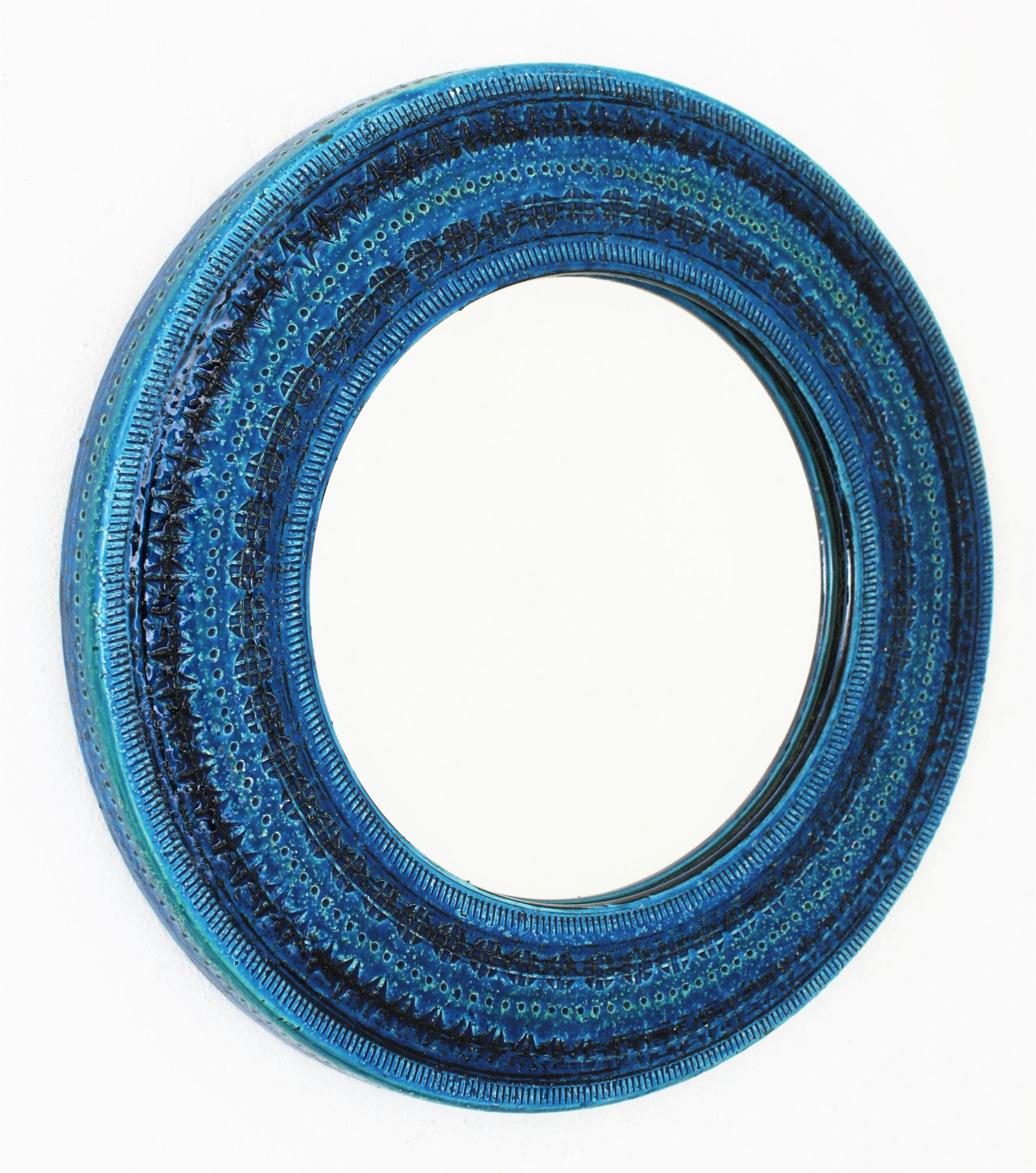 Italian Mid-Century Modern handcrafted blue terracotta glazed ceramic circular mirror with hand carved geometric designs in a vibrant turquoise and cobalt blue colors. Rimini blue collection designed by Aldo Londi for Bitossi. Italy, 1960s. 
Glass