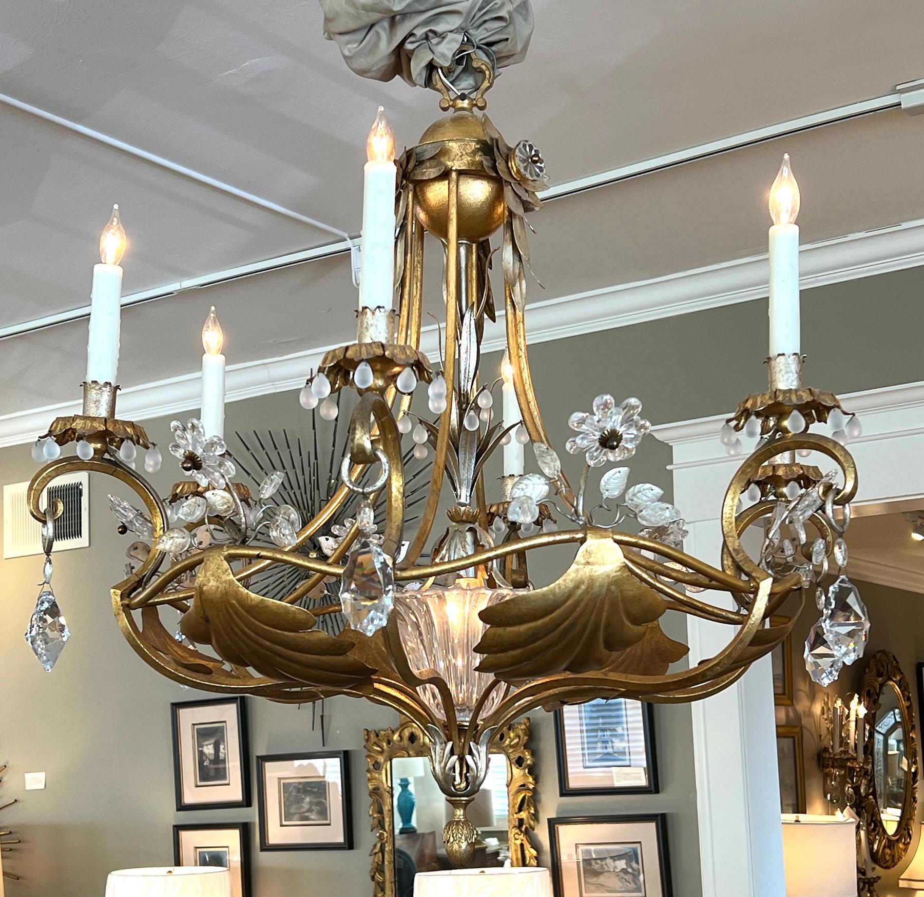 il lampadario traforato è sormontato da un elemento sferoide che sostiene sei bracci di candele a volute; il tutto è unito da un'elegante trave esterna; ornato da teste di fiori e foglie di cristallo intervallate da foglie di tole in scala, il tutto