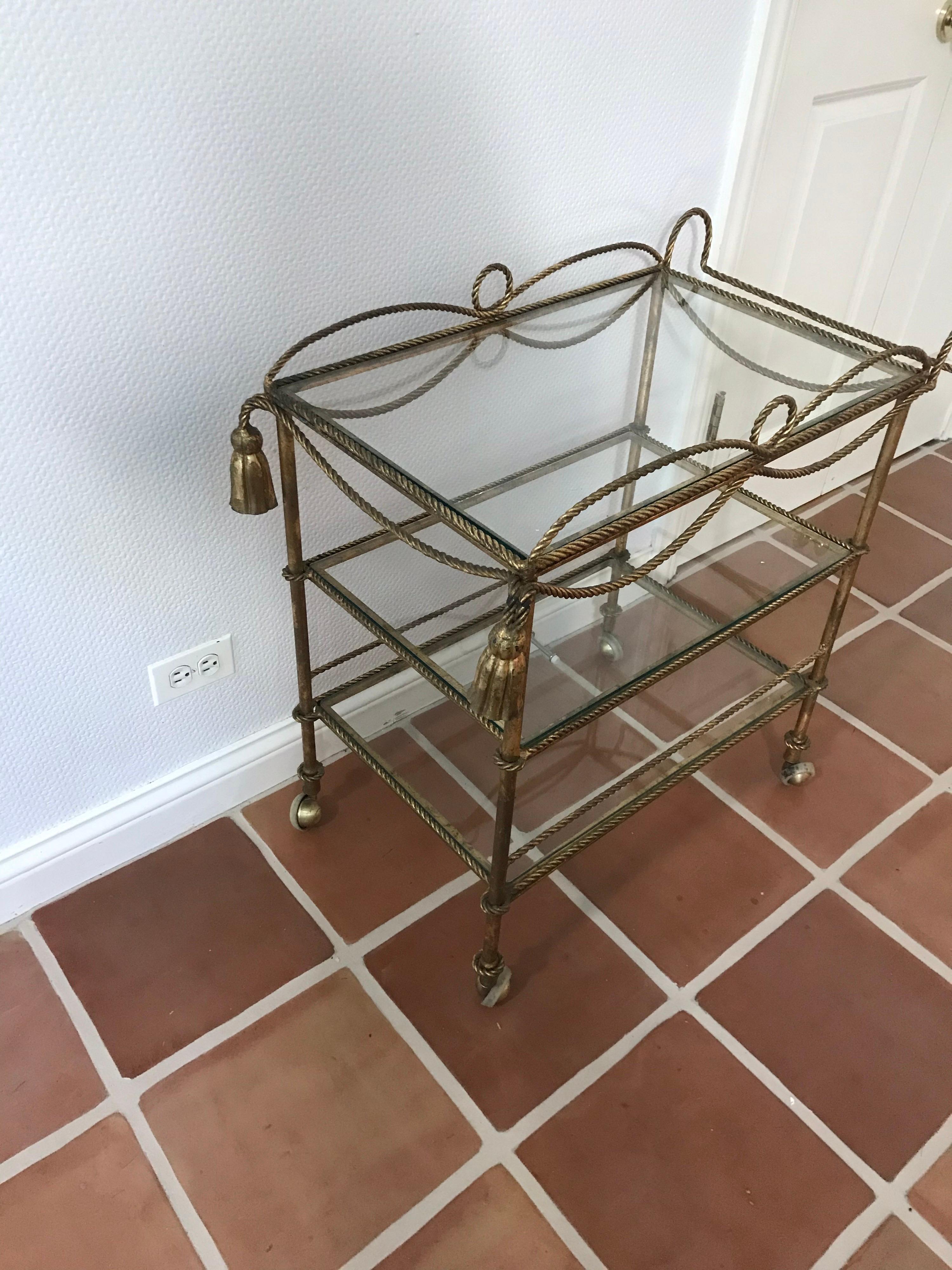 This is a 1960s gilt metal rope and tassel Italian bar cart on castors.