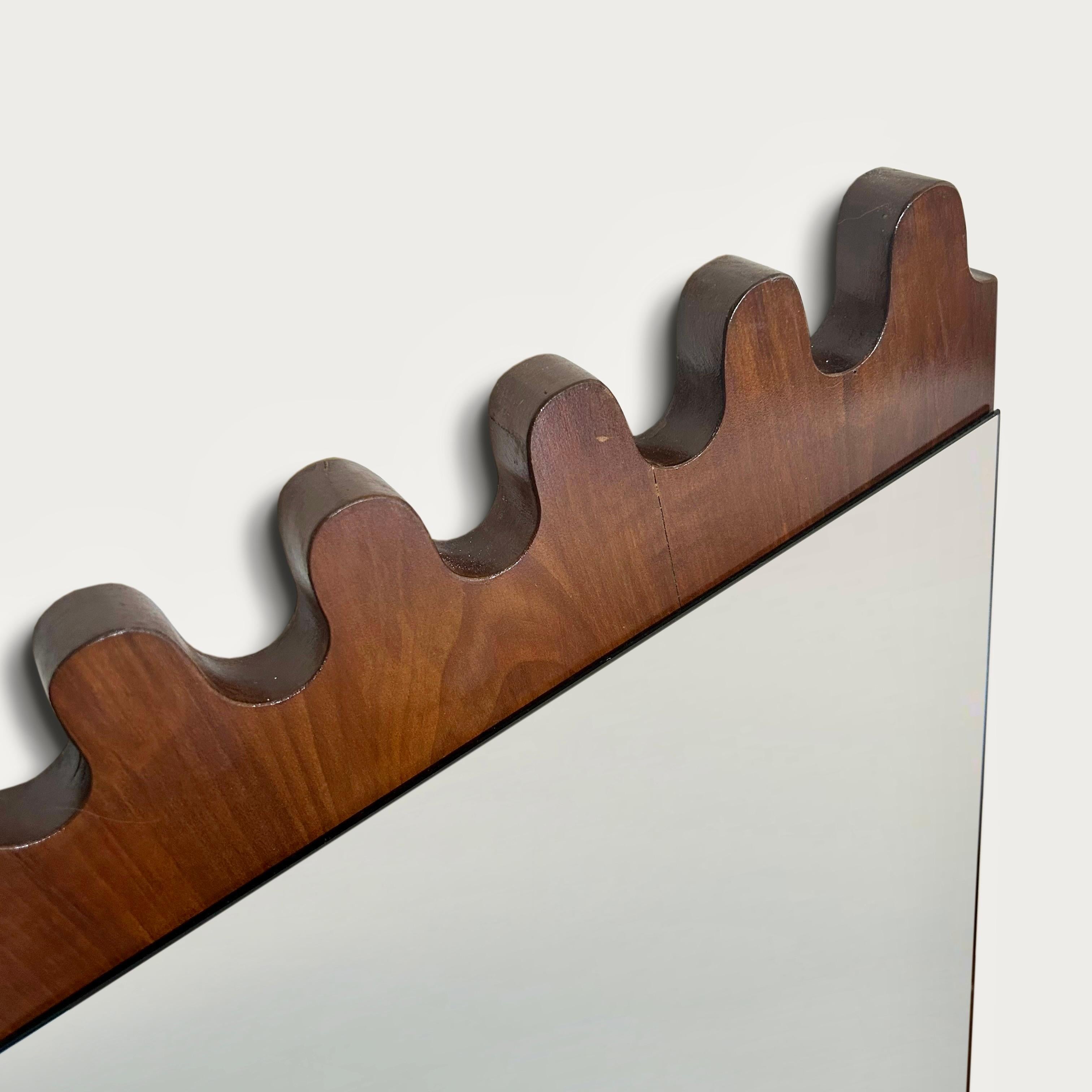 A pair of Italian 1960s wall mirrors with an undulating stylised cut out frieze to the top and bottom in stained cherrywood. 