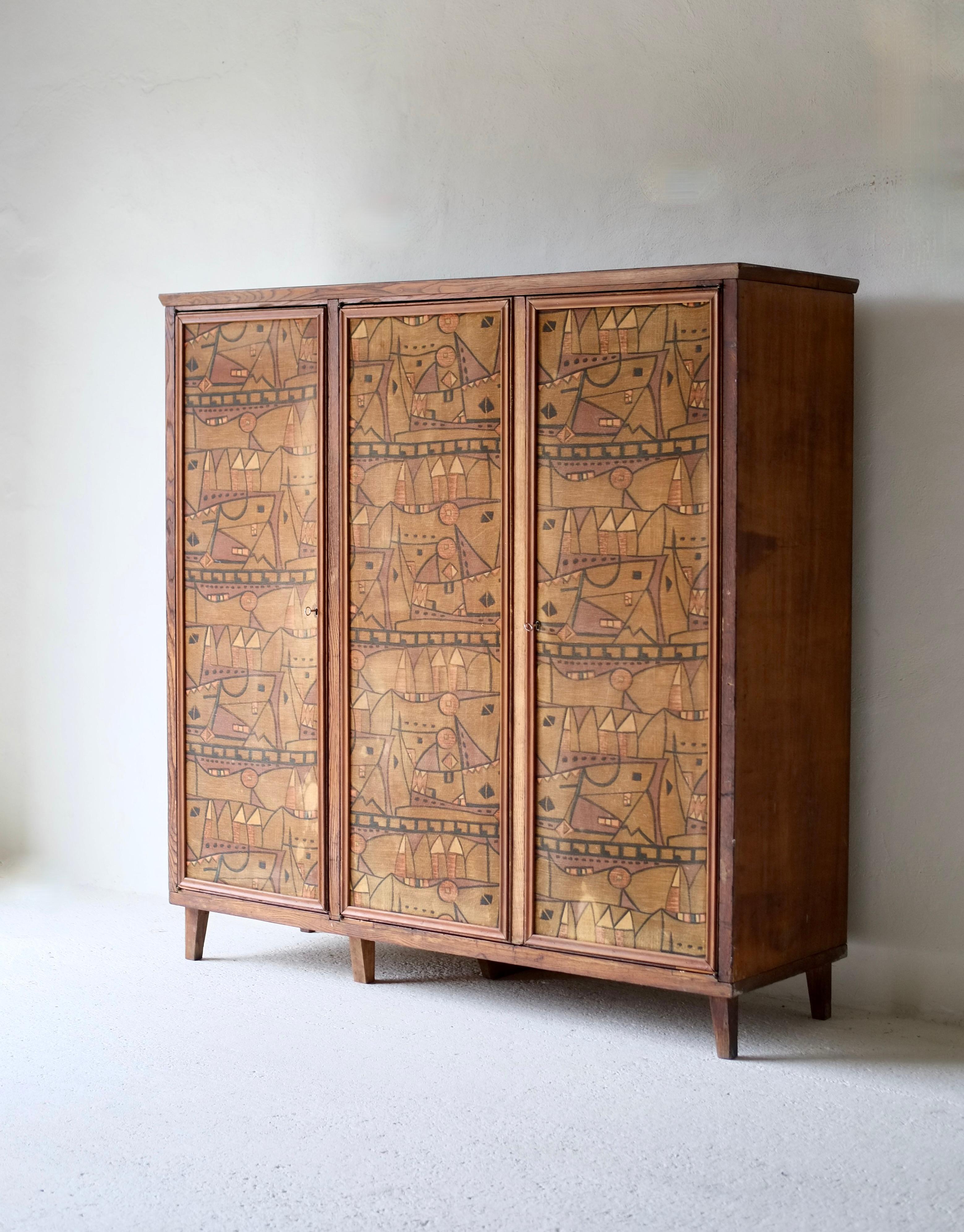 Un esclusivo armadio a tre ante con ante decorative in tessuto astratto. 

Italia, circa anni '60. 

Due piccole macchie di usura sul tessuto (vedi foto). 

H. 179 L. 178 P. 56,5 cm