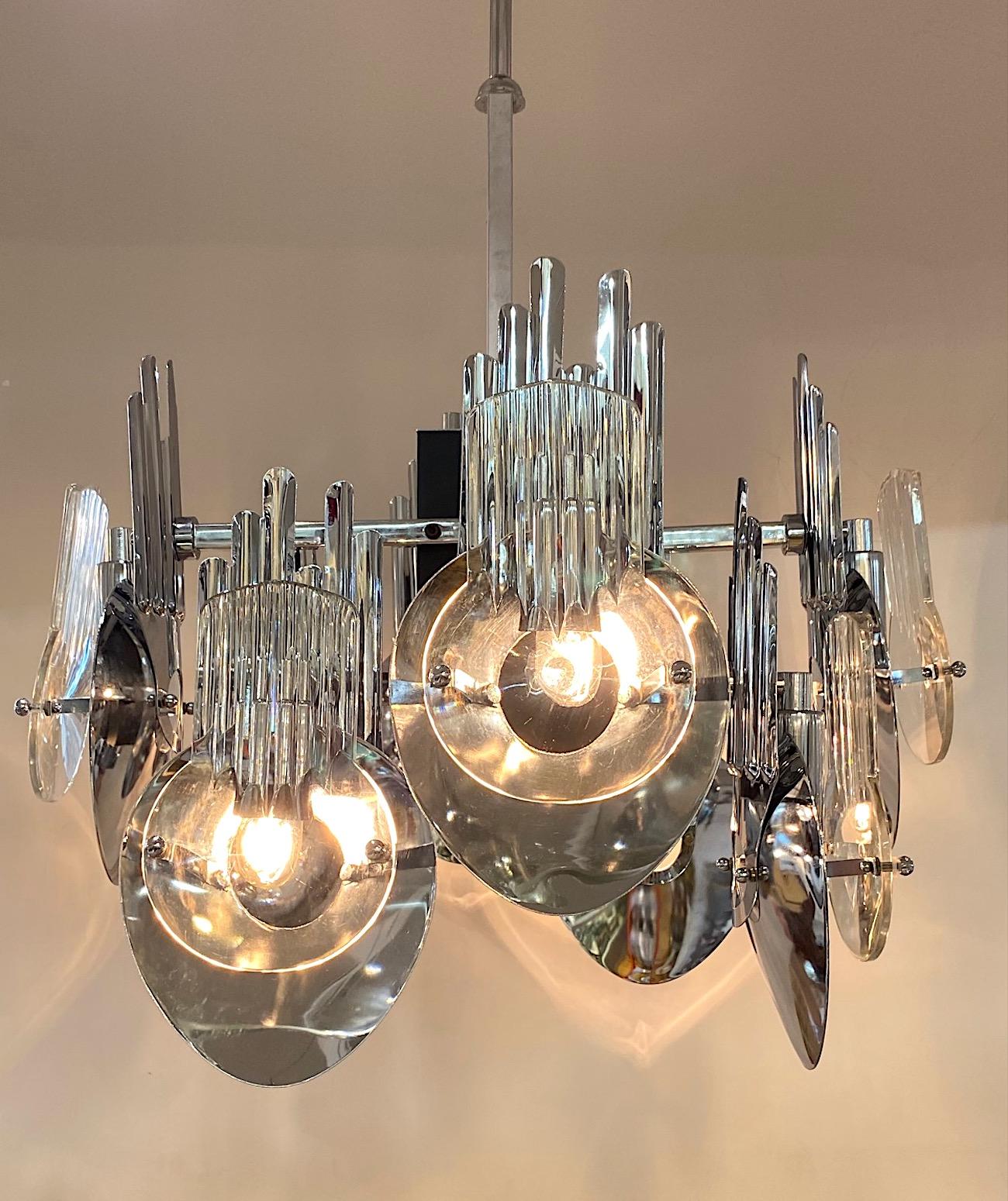 An abstract sculptural Italian chandelier circa 1970. The chrome frame has geometric design elements with the use of a square central column, square arms and abstract chrome back plates. Each plate has a round hole cut out for light. In between the