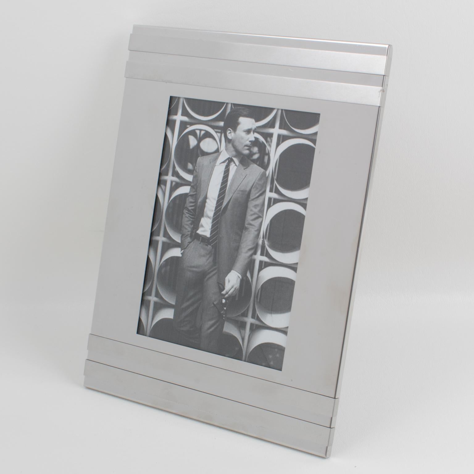 Sophisticated 1970s Italian modern picture photo frame. Rectangular shape with geometric design in shiny and brushed silver aluminum. Back and easel in black paper with a textured pattern. No visible maker's mark.
Measurements:
Overall: 8.07 in.