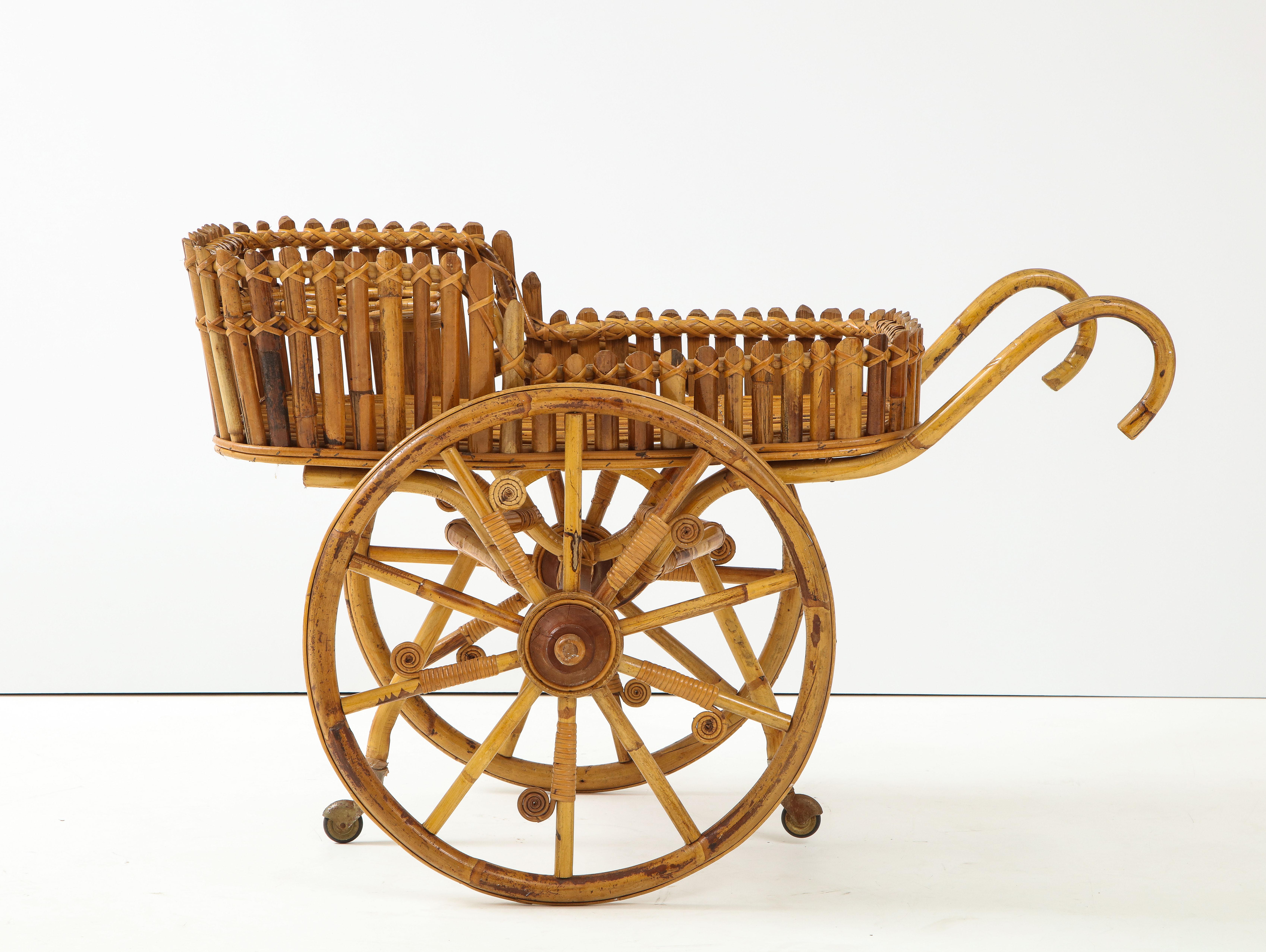 An Italian 1970's bamboo and wood bar cart with eight bottle holders, large storage basket, supported on two large wheels decorated with wood and bamboo swirls between the spokes. Move this piece around with its elegantly outstretched curved