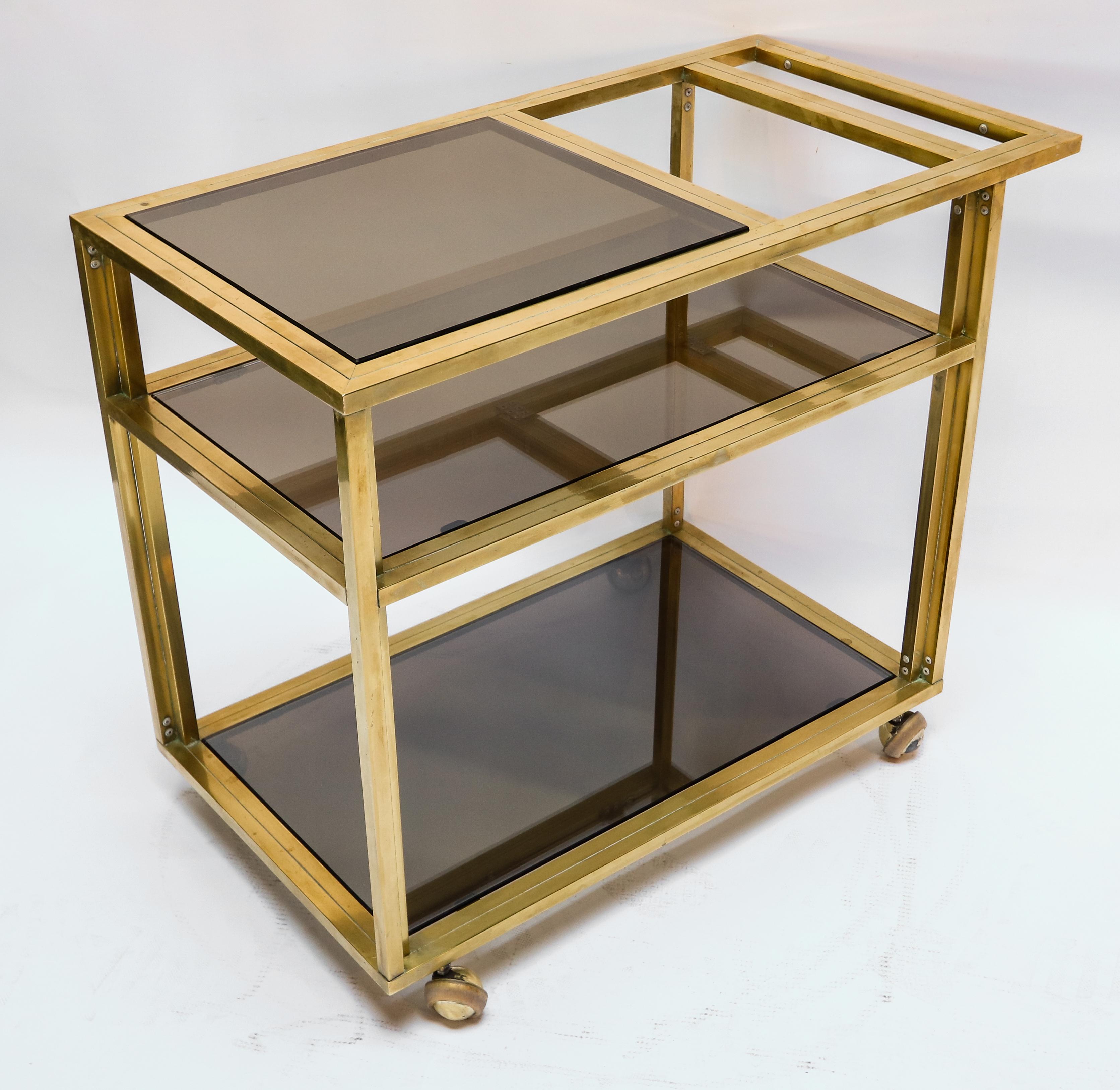 Italian brass bar cart with three smoked glass shelves from the 1970s. Half shelf on top accommodates large bottles on the second shelf.