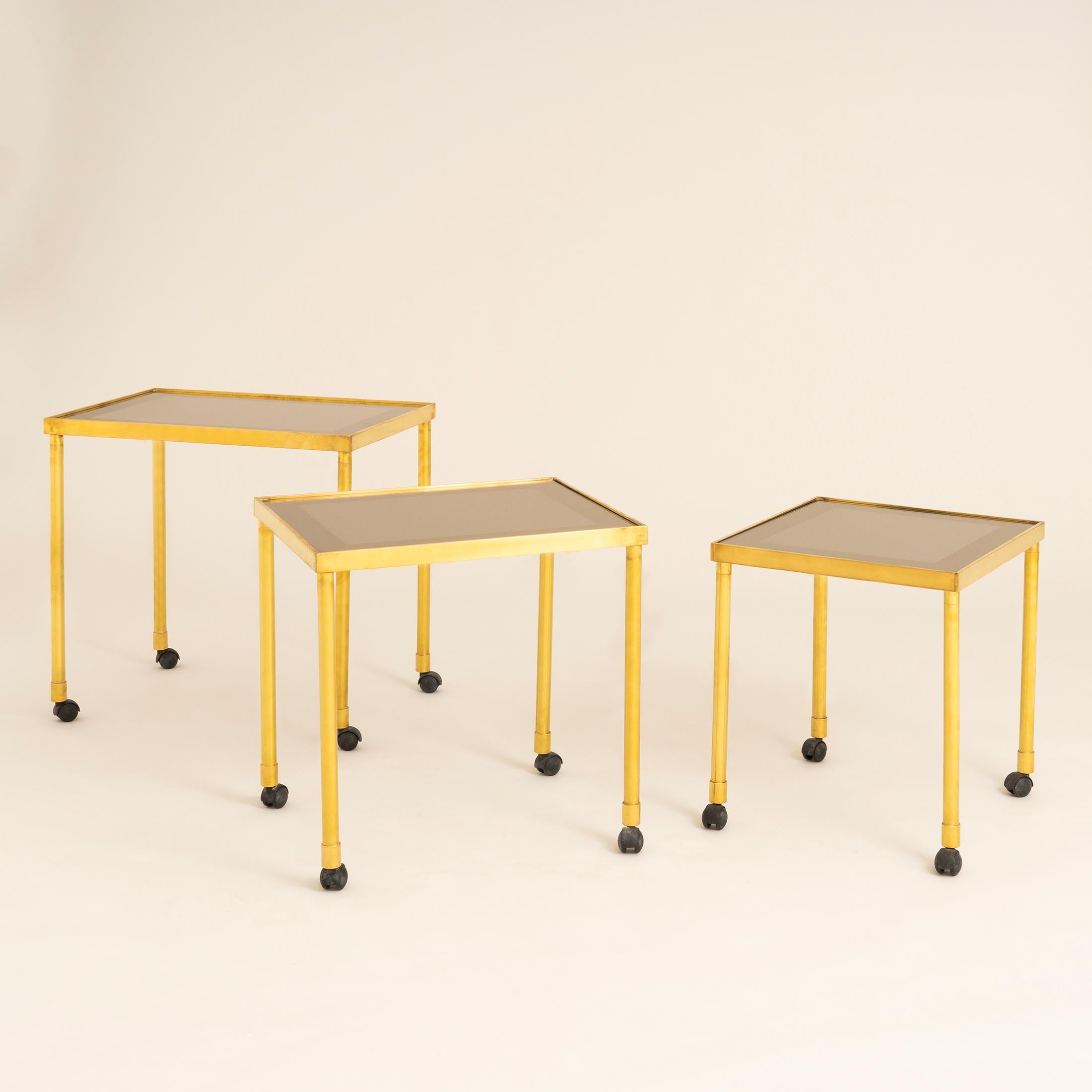 Nest of three brass Italian side tables each with a Smokey glass top with a mirror surround. Each table moves by castor wheels making them easy to spread around the room.