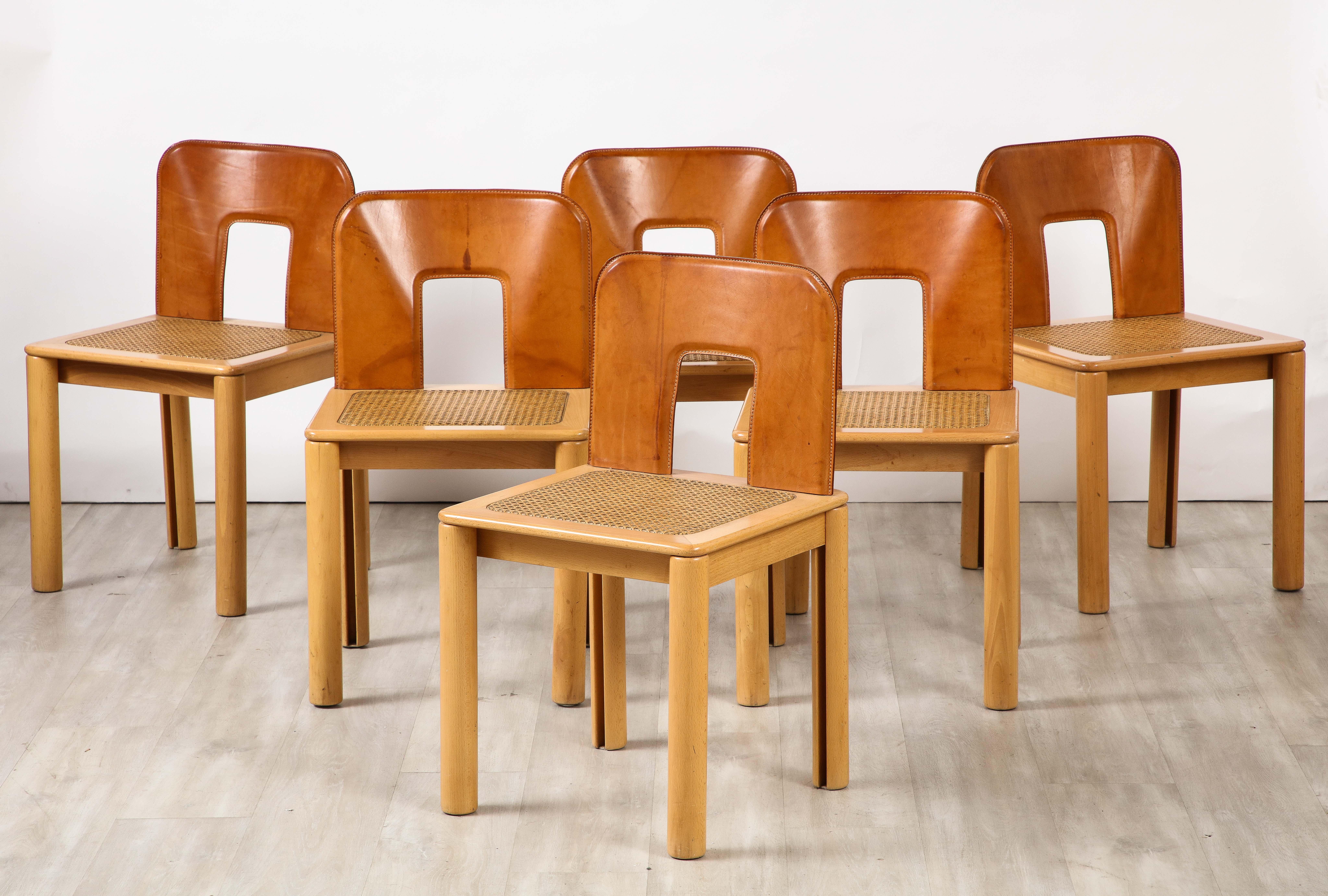 An Italian 1970's set of six side chairs or dining chairs with molded caramel leather back rests, caned seats and molded maple wood frames with rounded legs.  The combination of these three organic and textured materials create a charming and chic