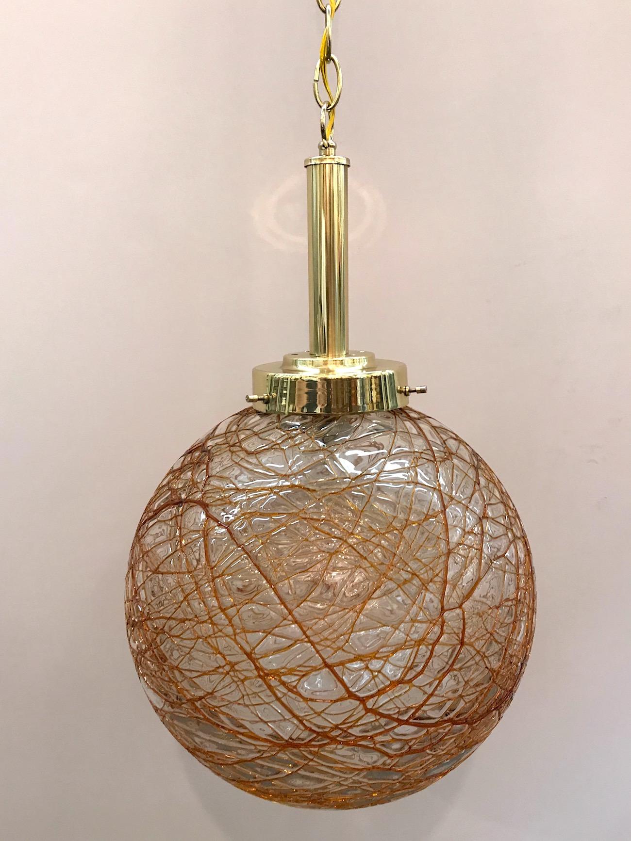 A lovely circa 1970s pendant light from Murano Italy. Globe shade of handblown clear glass with applied amber color glass splatter design. Brass mount, chain and original matching dome ceiling canopy. Diameter of globe is 12 inches. Pendant as