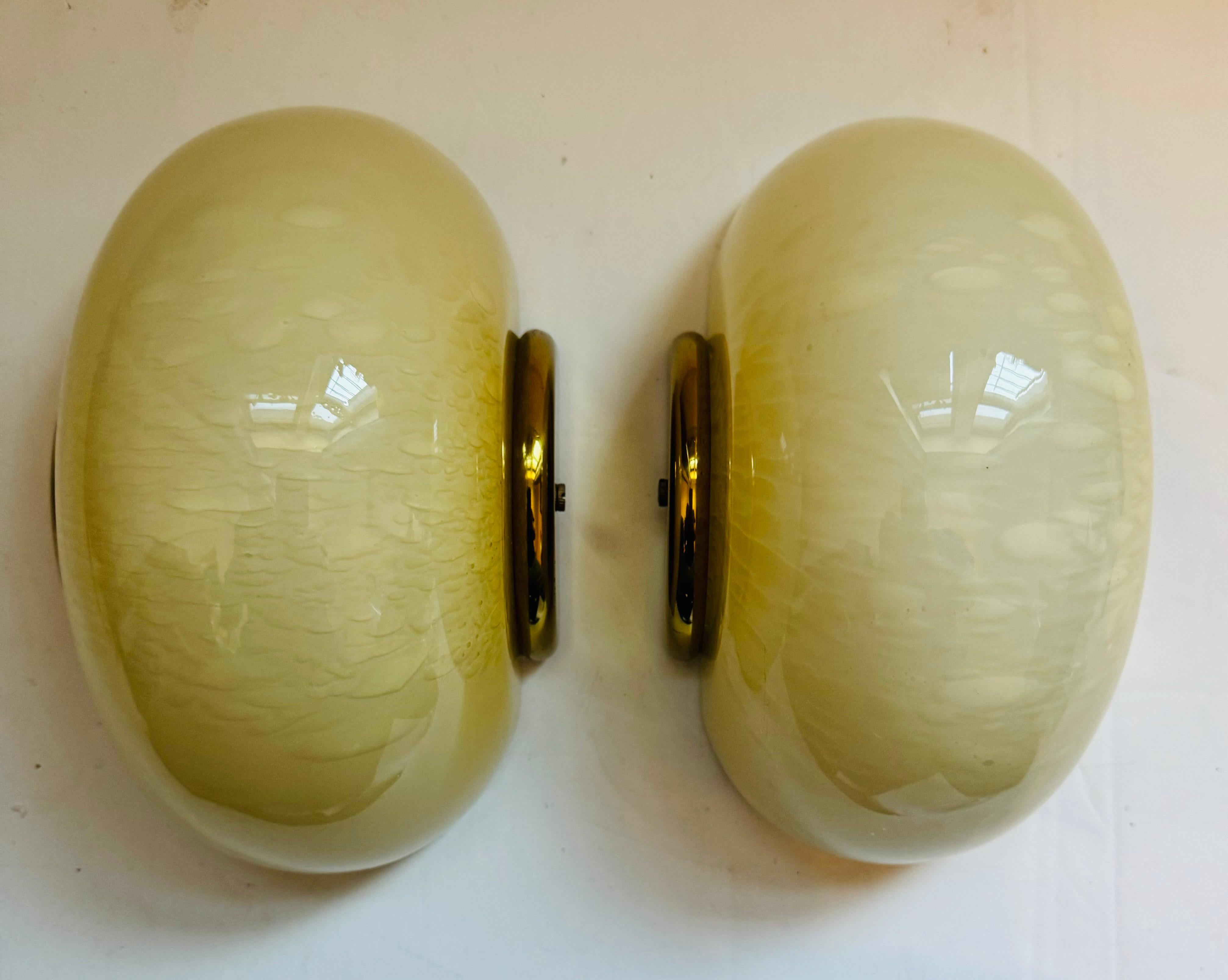 A handsome pair of light custard Murano egg shaped wall lamps with half moon brass fittings. 1970s Italian by lighting maker, Fabbian. Can be installed vertical or horizontal.