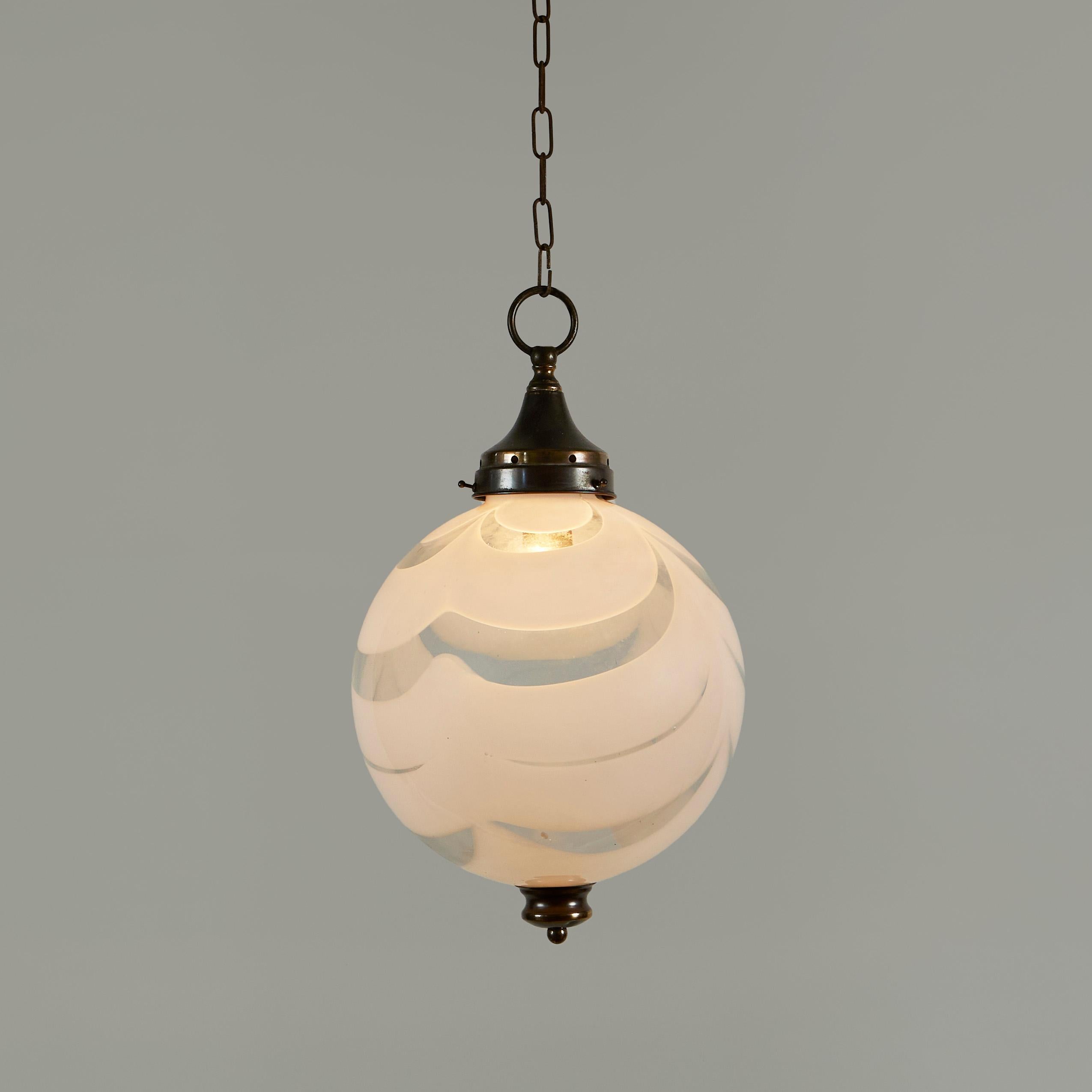 Murano handblown glass sphere pendant of transparent glass heavily patterned with thick swirls in white. Decorative brass fitting and ceiling rose.
