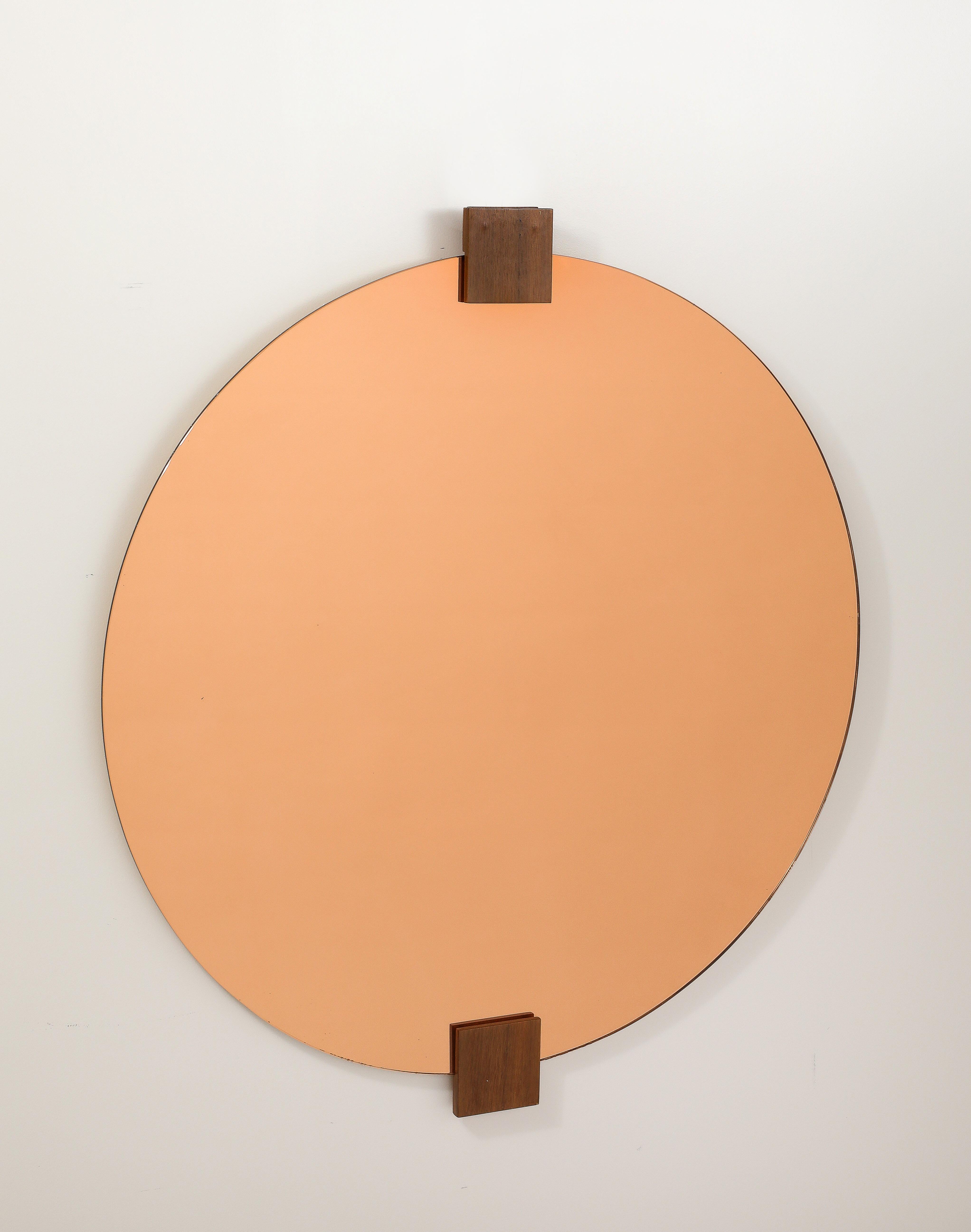 Impresionante espejo circular de cristal dorado rosa de los años 70 con decoración de bloques de madera en la parte superior y la base;  este espejo elegante y exquisito es una obra de arte escultural, grandiosa e impresionante en escala y colorido.