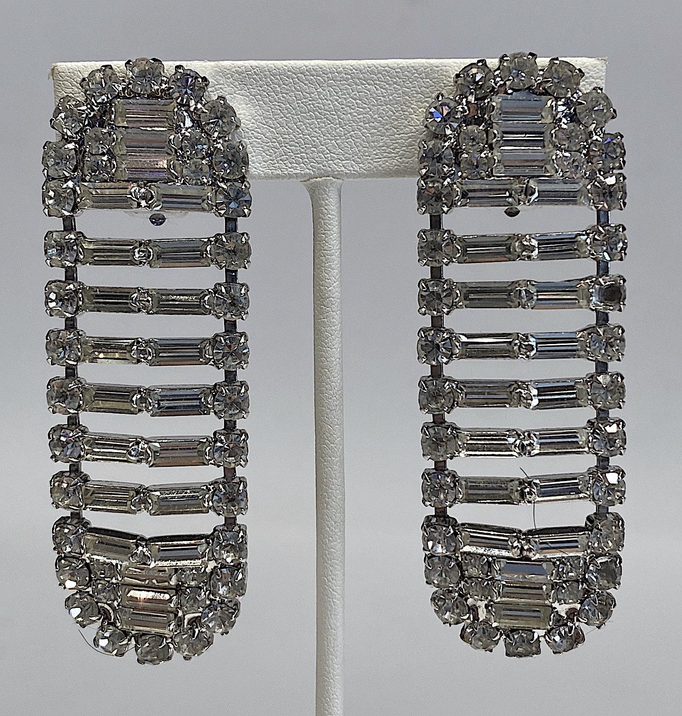 A sparkles and noticeable pair of Italian round and baguette rhinestone earrings from the 1980s. The earrings are large yet constructed with open spaces to keep them light and delicate in appearance. The metal is rhodium plated. Each earring has a