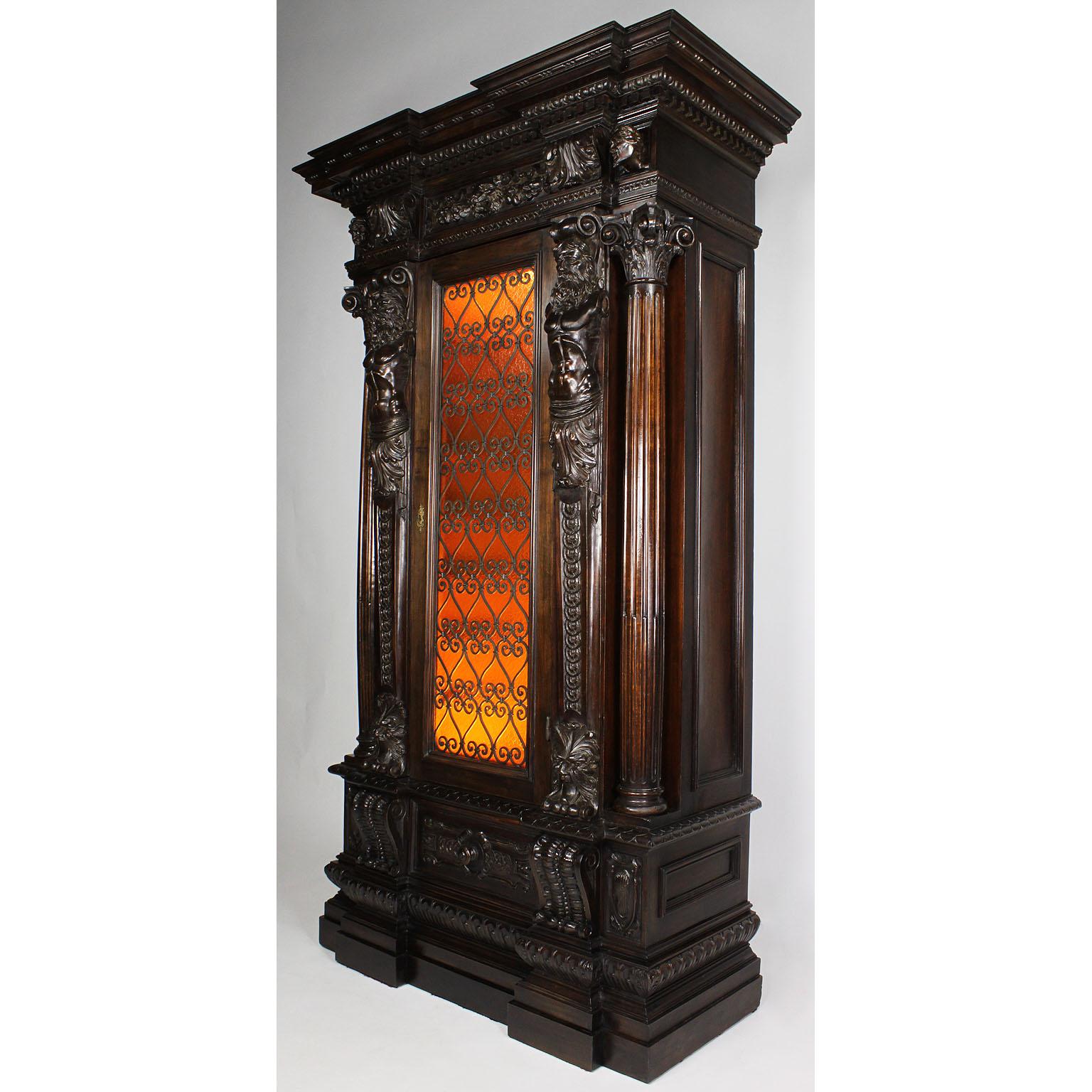 A fine Italian 19th-20th century Baroque Revival style carved walnut figural wine - storage cabinet. The elongated carved body centered with a single door with an amber glass inset and a wrought iron grill decoration, concealing eight interior