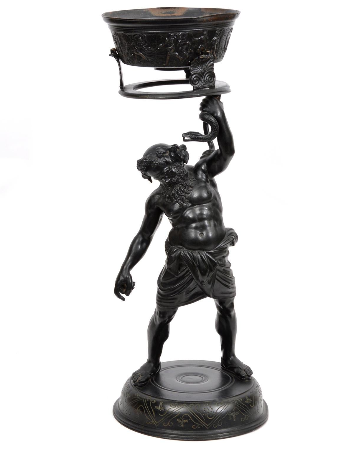 Standing 26 inches tall this two part Italian Grand Tour patinated bronze statue depicts Silenius, the Roman good of wine, holding up a snake footed ceremonial vessel. It is unusual to find this statue with the accompanying vessel which in this case