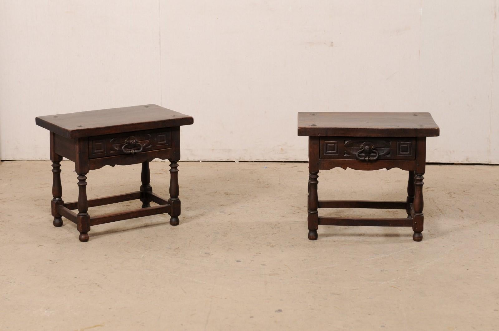 An Italian pair of carved-walnut side tables with drawer from the 19th century. This antique pair of tables from Italy each have a thick walnut slab top with hammered iron nail-heads at each of the four corners, which overhangs the apron below that