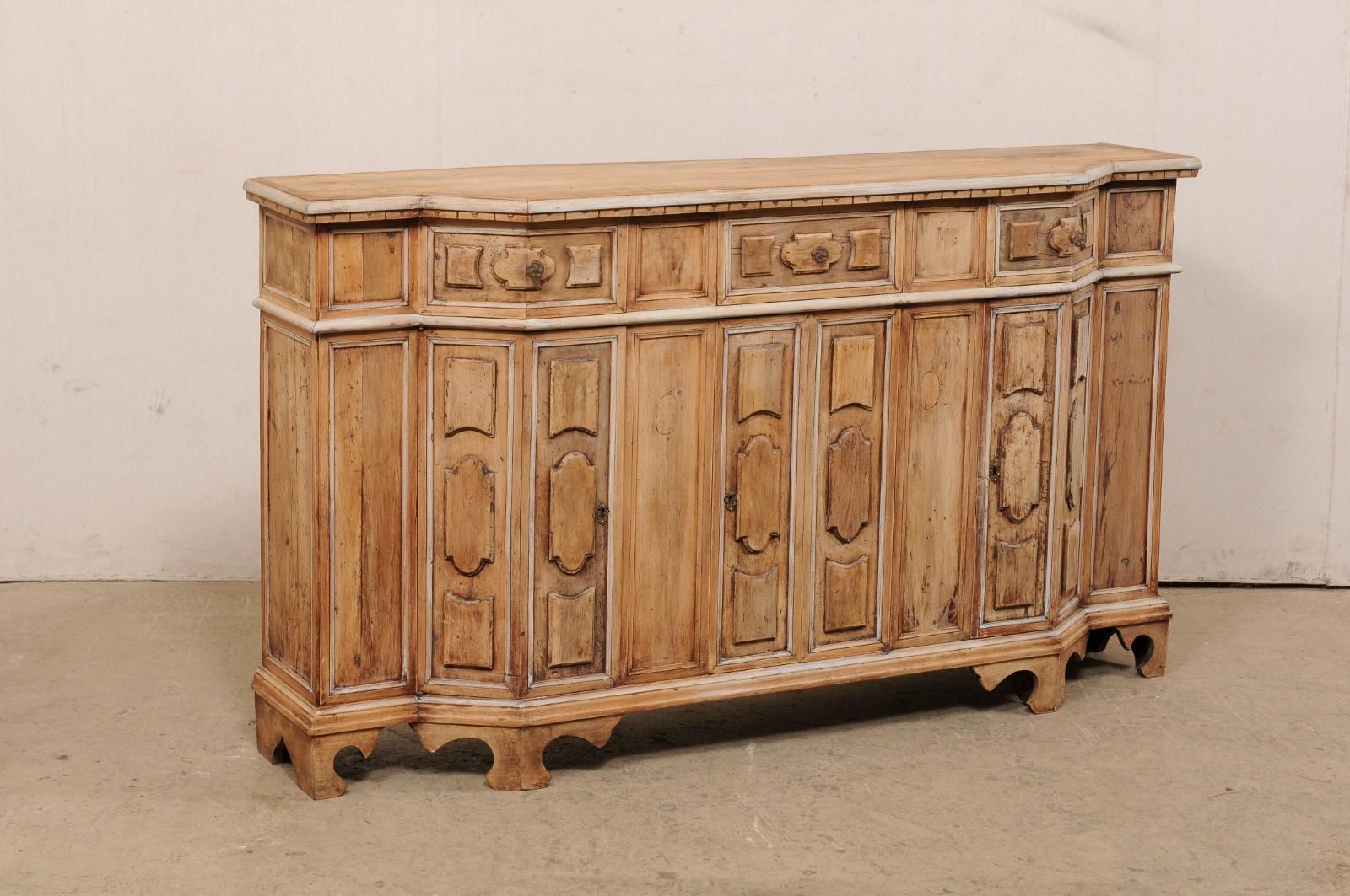 An Italian buffet cabinet with decoratively raised panels, from the 19th century. This antique console cabinet from Italy has a canted breakfront design, houses three smaller drawers atop three doors, and is raised on shapely-carved bracket style