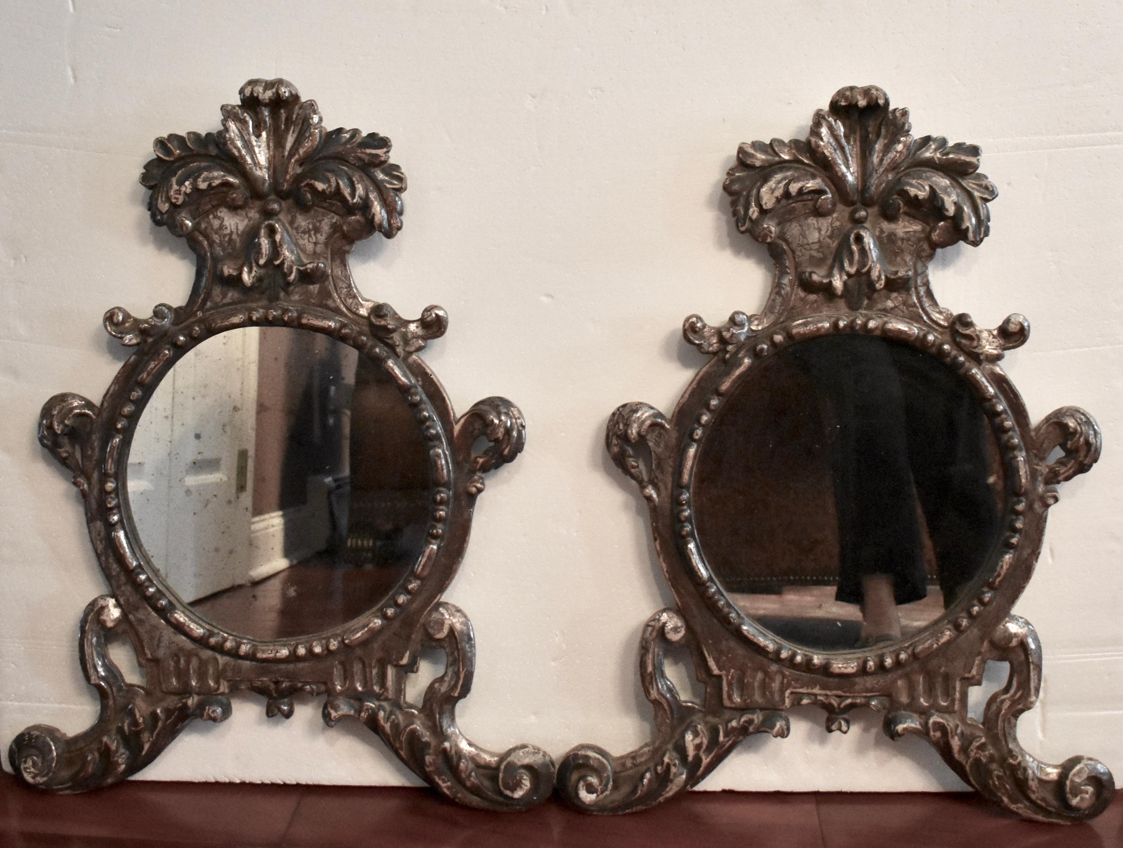 An unusual pair of silver-giltwood wall mirrors in the Baroque Taste, Italy, circa fourth quarter of the 19th century.

Topped with leaf-carved crests, the oval mirror plates are framed with beading, and sit on scrolled, leaf-carved and pierced